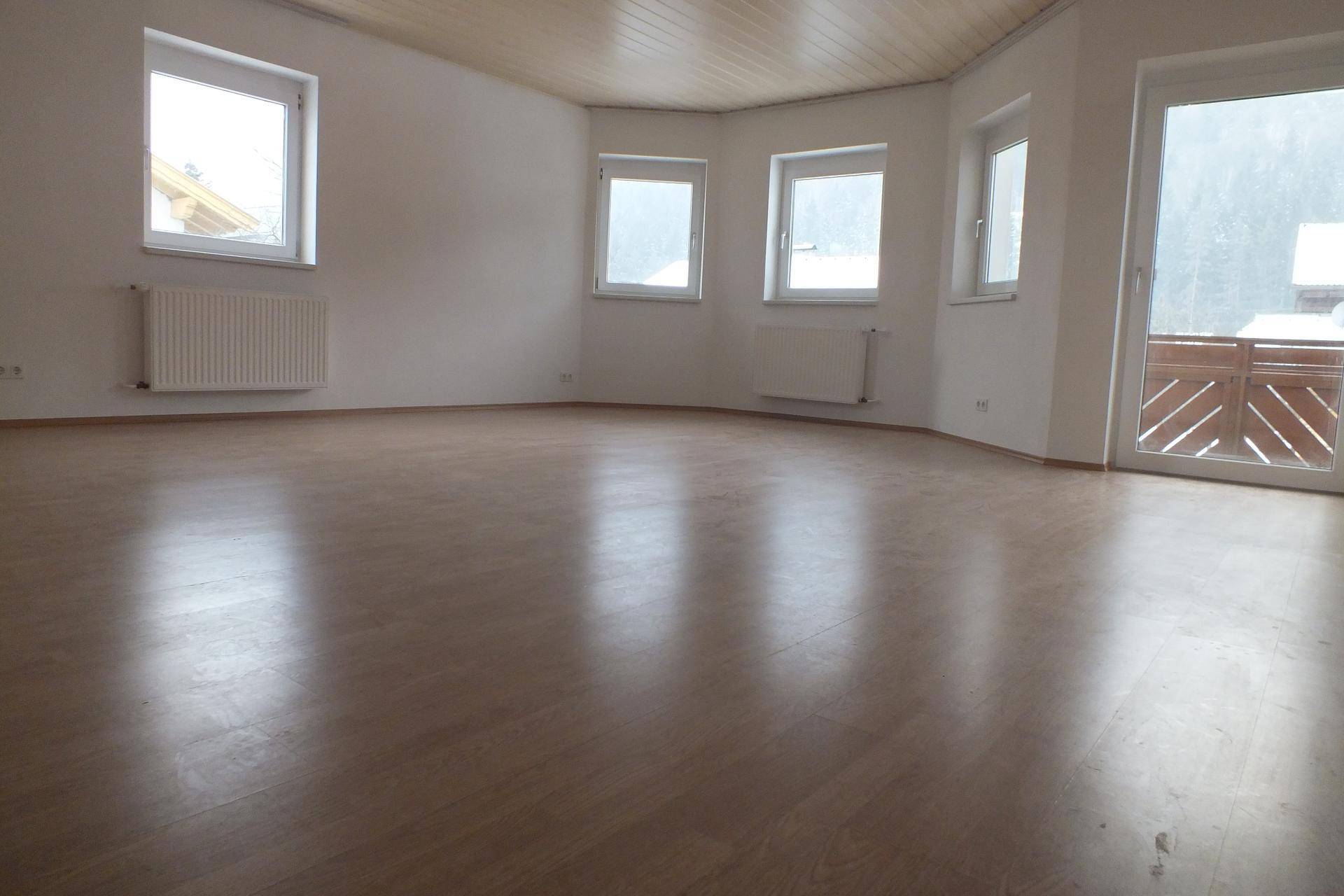 Geräumiges Wohnzimmer mit Laminatboden, vielen Fenstern und Zugang zum Balkon.