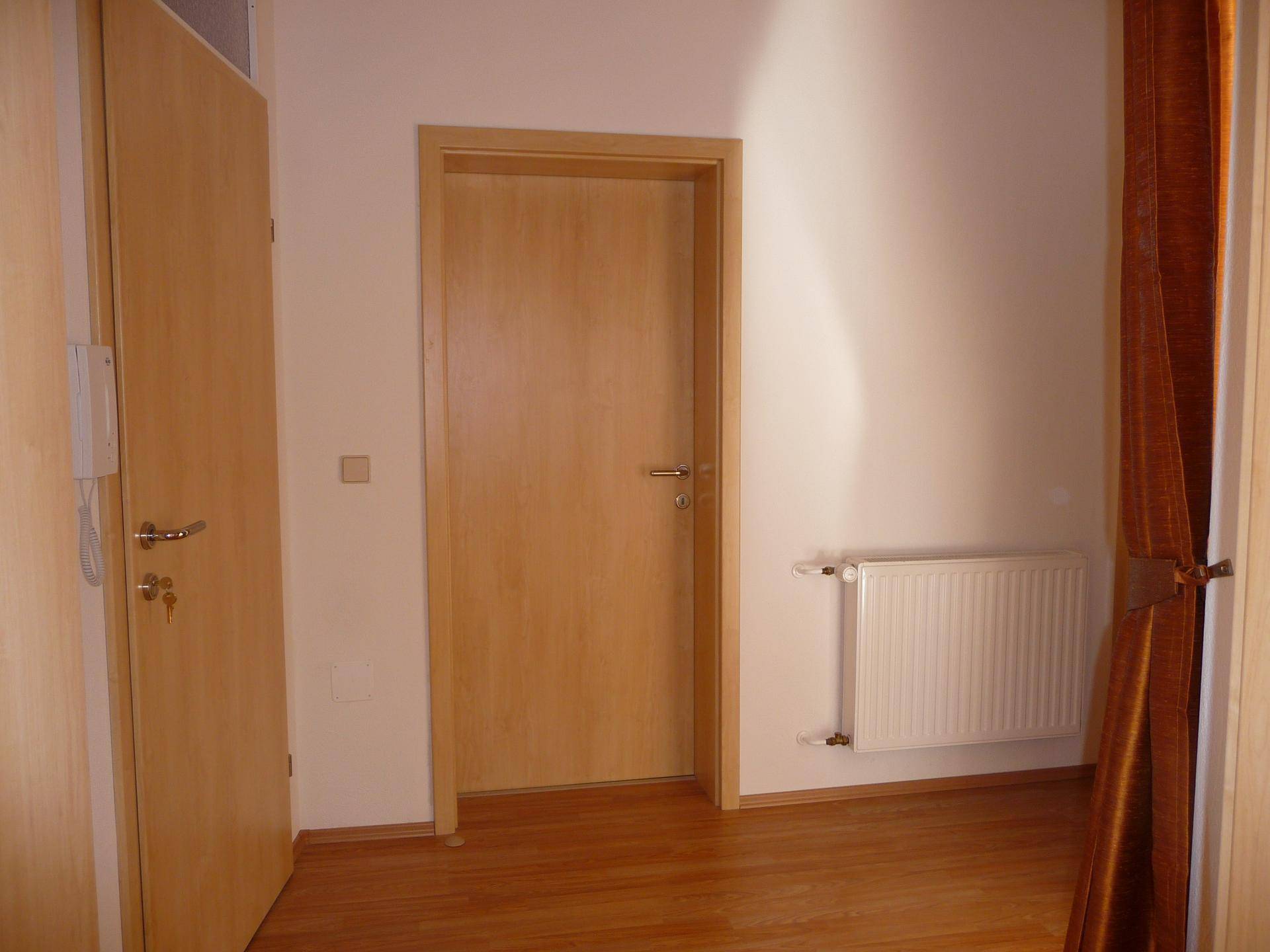 Heller Flur mit Holztüren, Laminatboden und Heizkörper.
