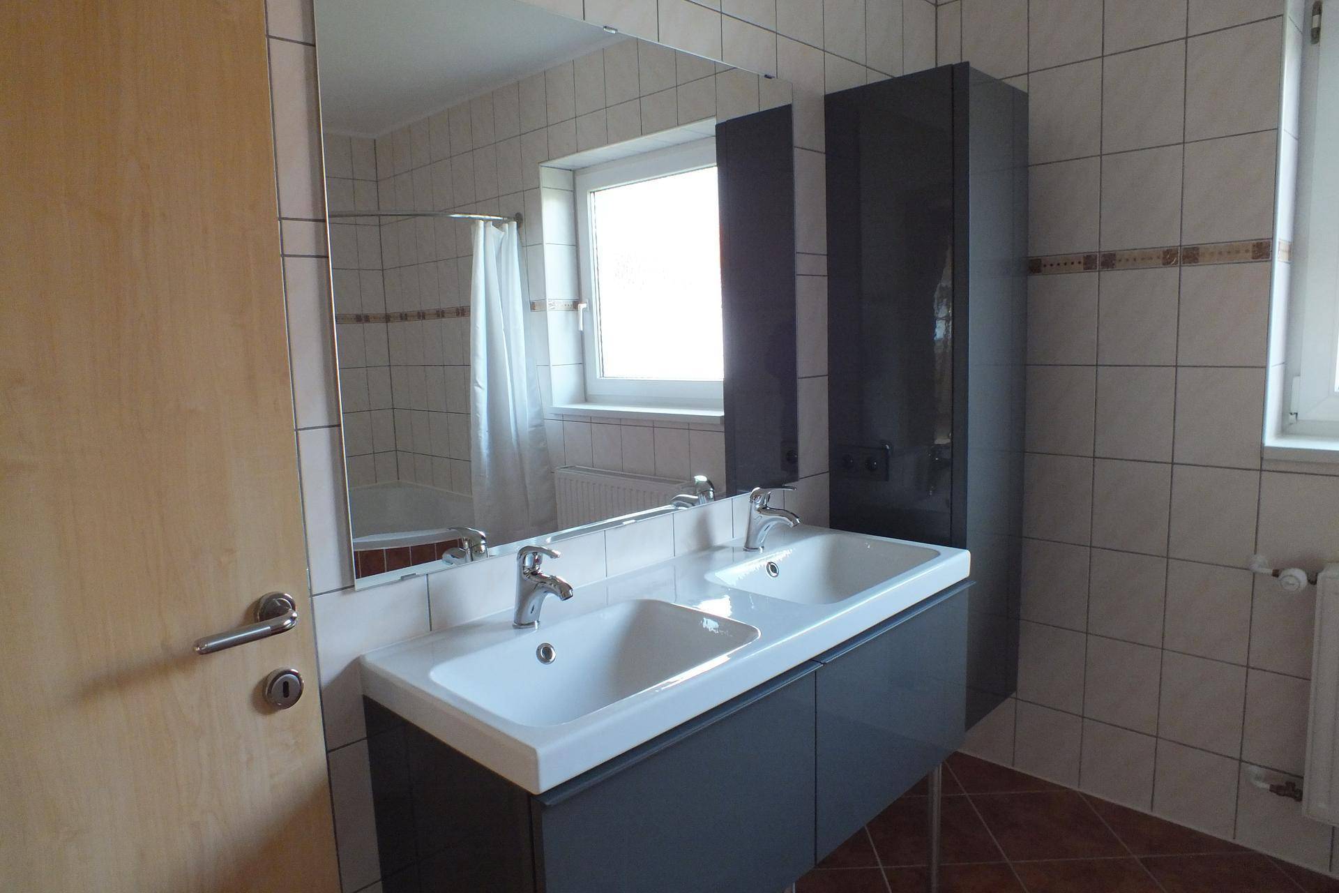 Modernes Badezimmer mit Doppelwaschbecken, großem Spiegel und Fenster.