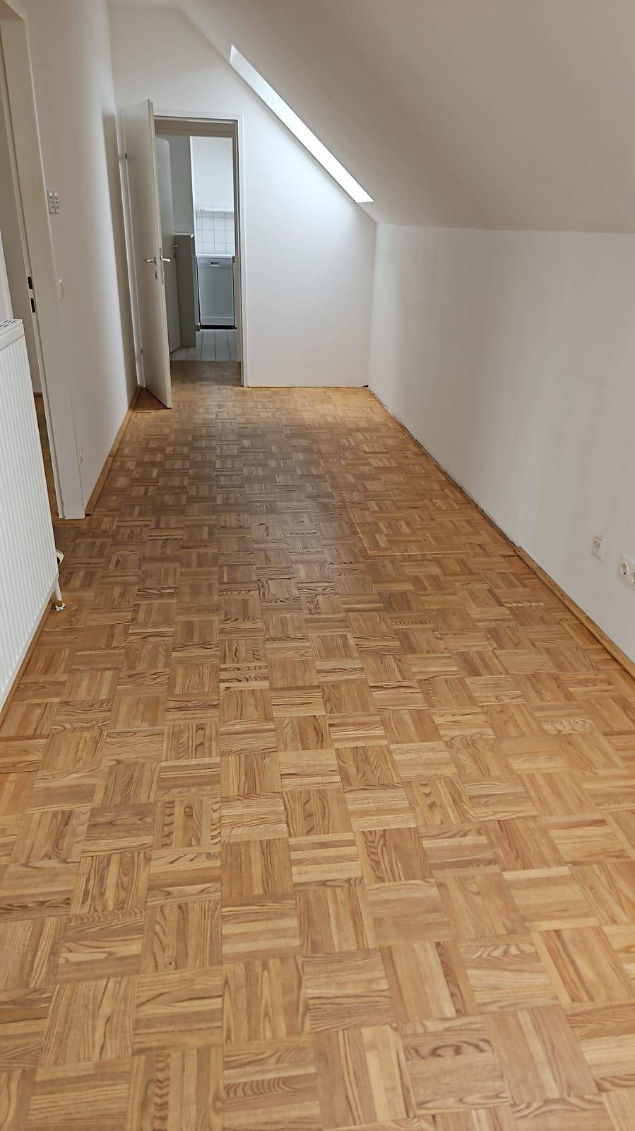 Leerer Büroraum mit Holzparkett und Dachschräge, ideal für ein ruhiges Arbeitsumfeld.