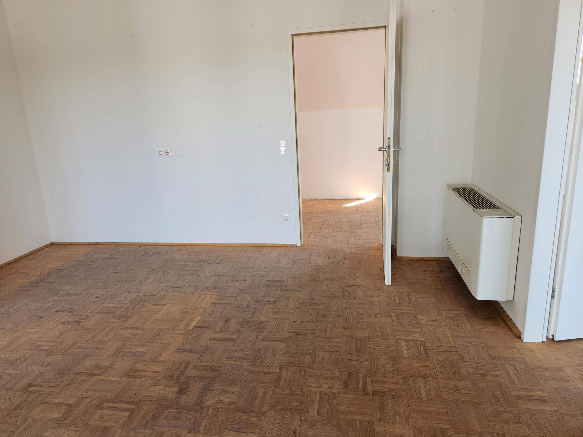 Geräumiger Büroraum mit Holzparkett und Heizkörper an der Wand, bereit zur individuellen Gestaltung.
