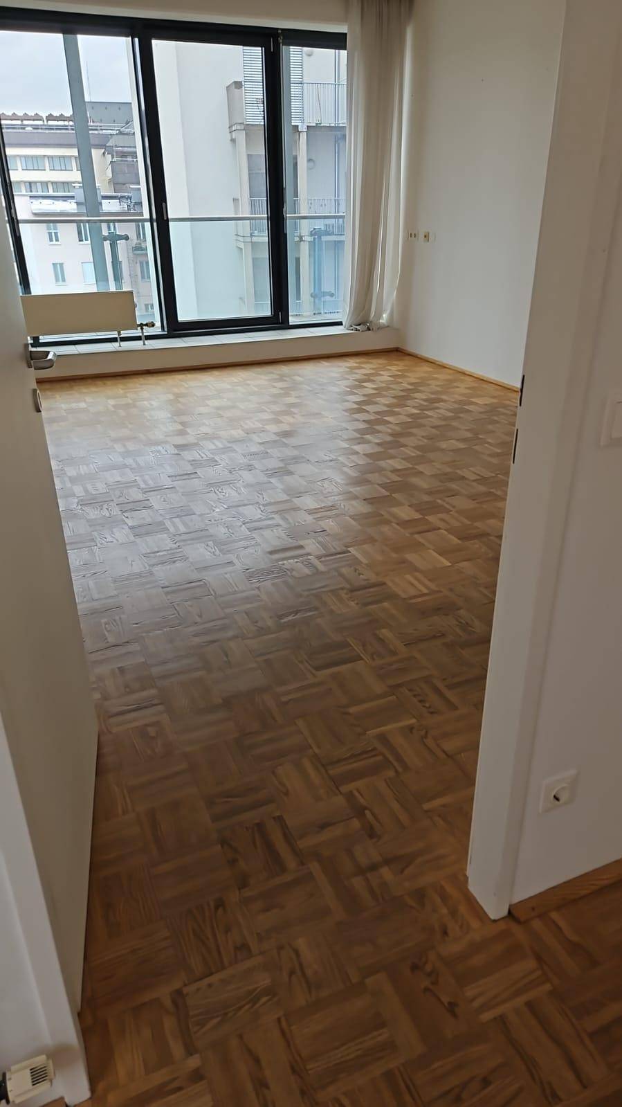 Heller Büroraum mit Fischgrätparkett und bodentiefen Fenstern, die einen Stadtblick bieten.