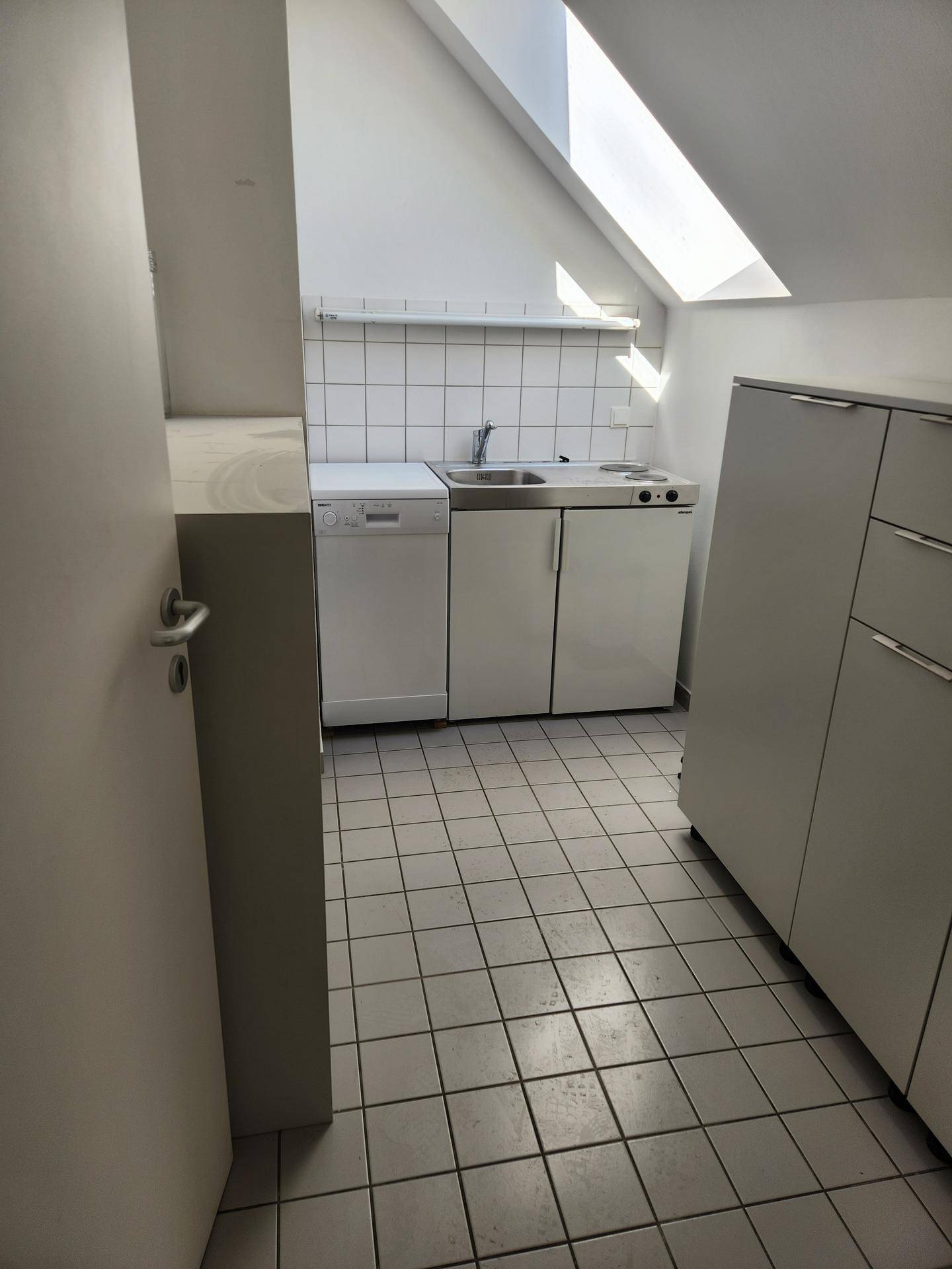 Kleine Küchenzeile mit Spüle, Kochfeld und Geschirrspüler unter einer Dachschräge.