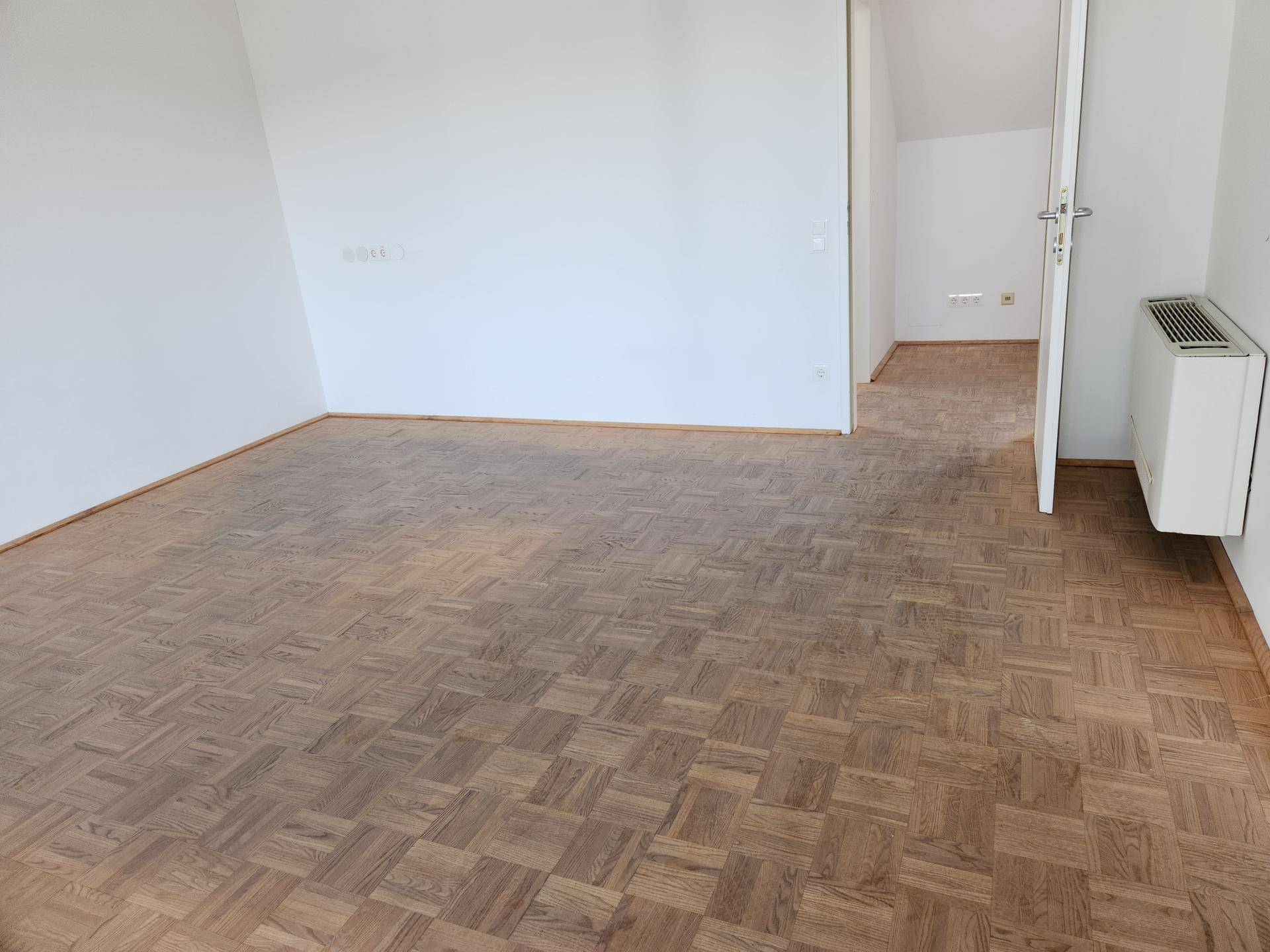 Leerer Büroraum mit Holzparkett und weiß gestrichenen Wänden, ideal für flexible Nutzung.