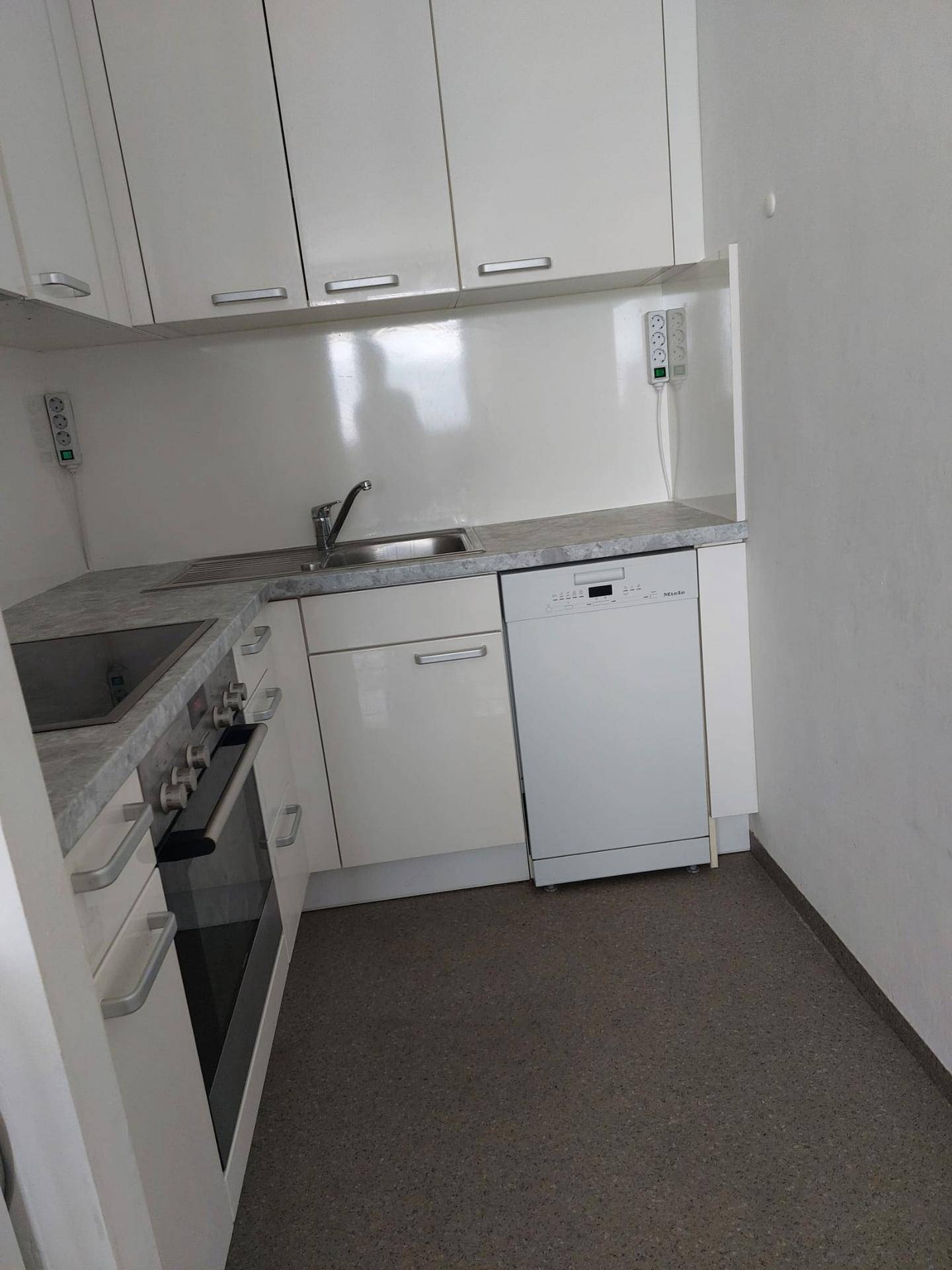 Kleine Einbauküche mit weißen Schränken, grauer Arbeitsplatte und integriertem Geschirrspüler.