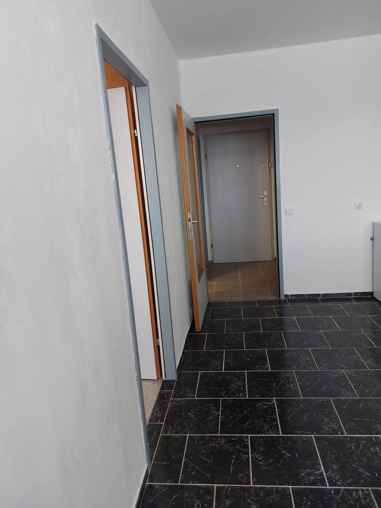 Heller Flur mit dunklen Fliesen und mehreren Türen, der verschiedene Räume verbindet.