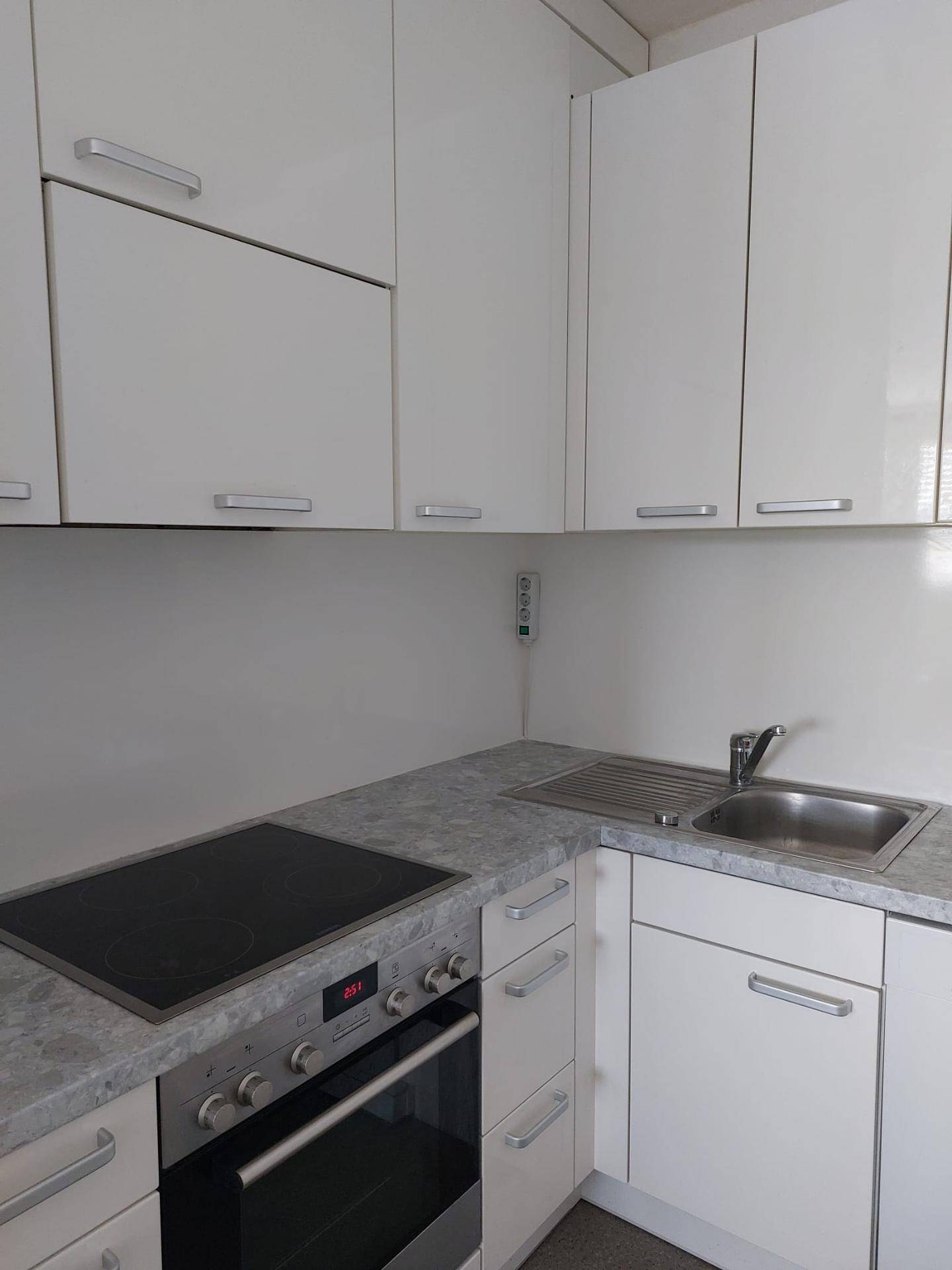 Detailansicht der Küche mit Induktionskochfeld, Backofen und Spüle in weißen Schränken.