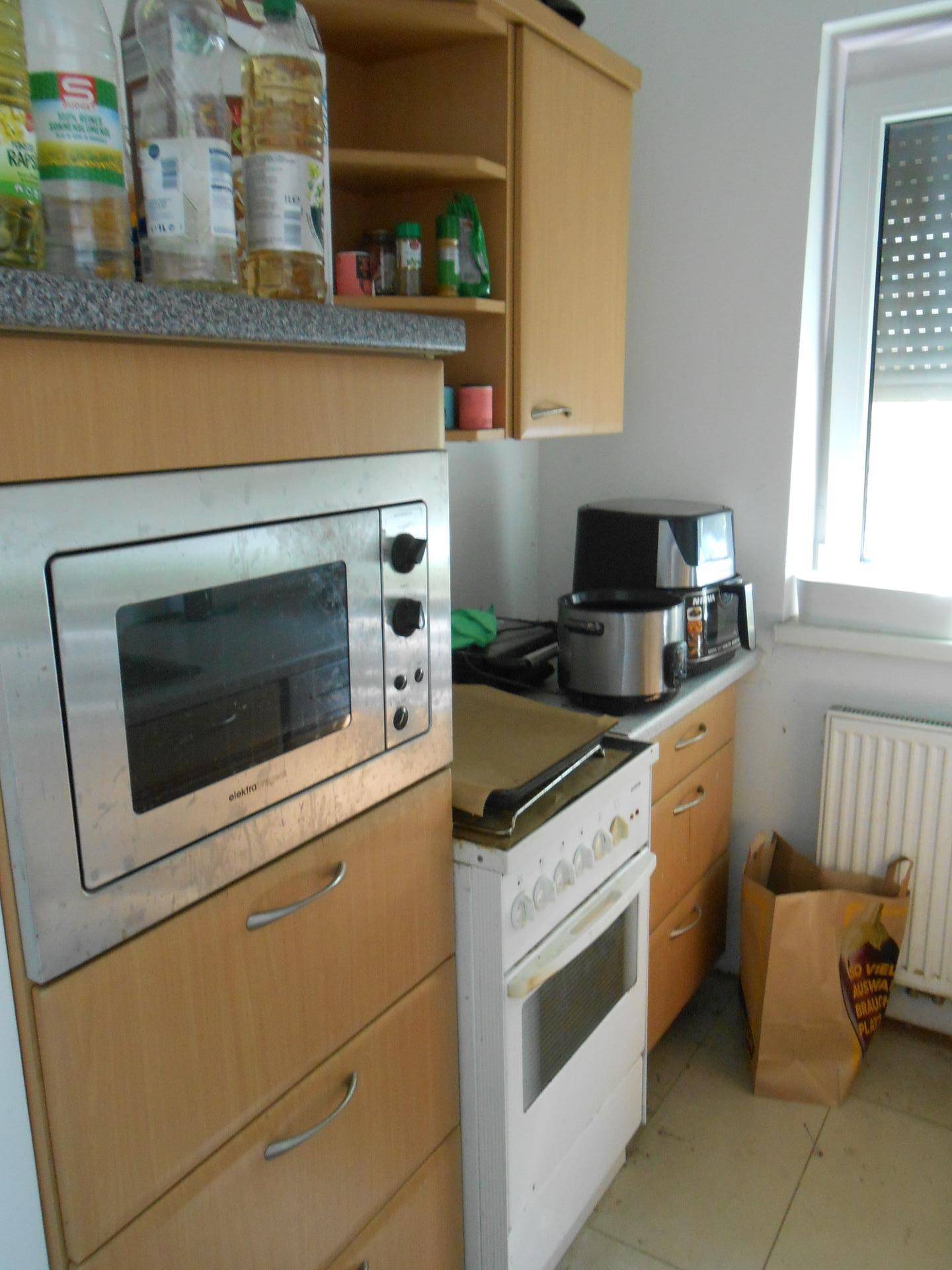 Funktionale Küche mit Holzschränken, Mikrowelle und Herd in hellem Raum.