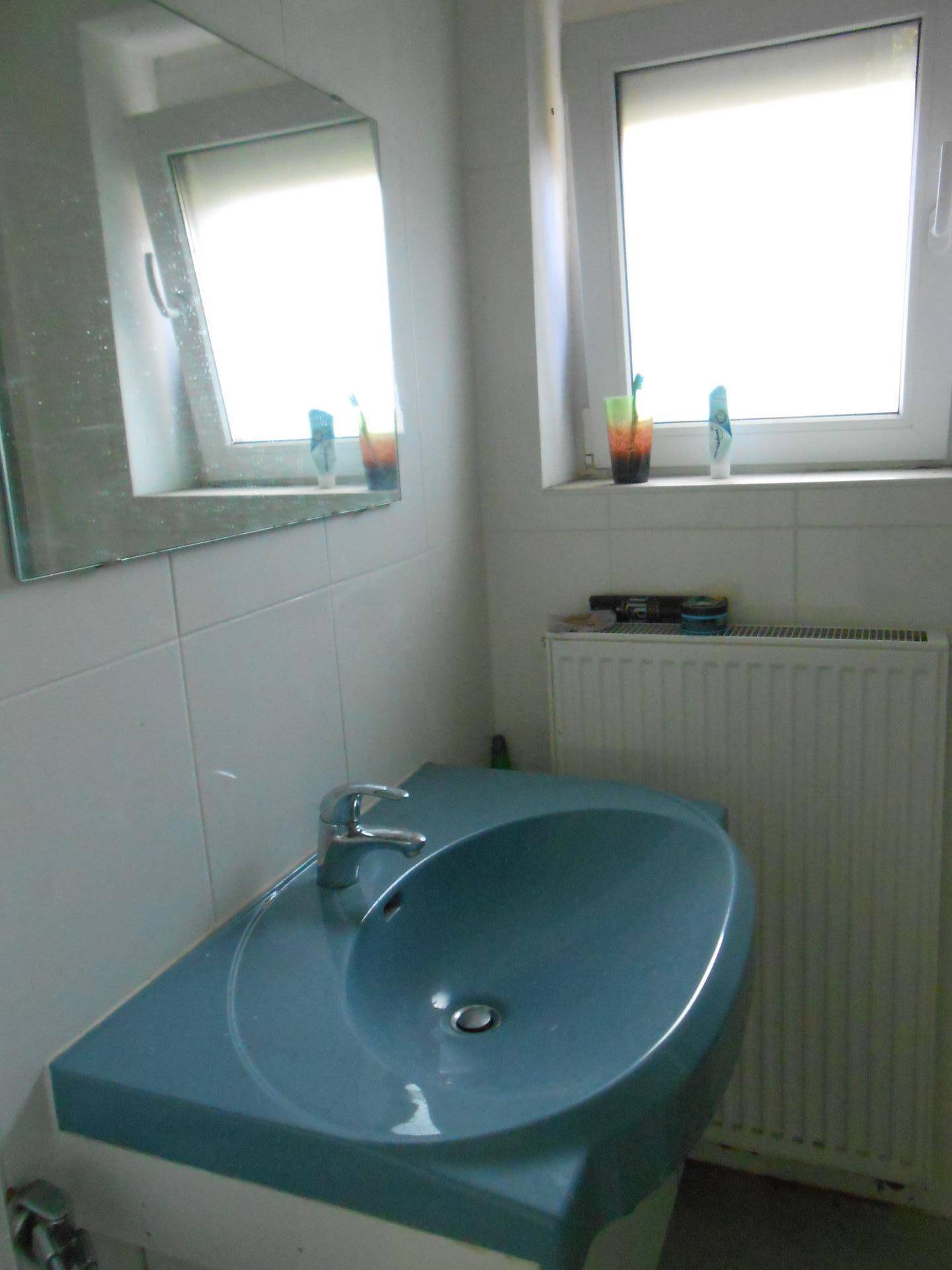 Badezimmer mit hellblauem Waschbecken, Spiegel und Fenster für Tageslicht.