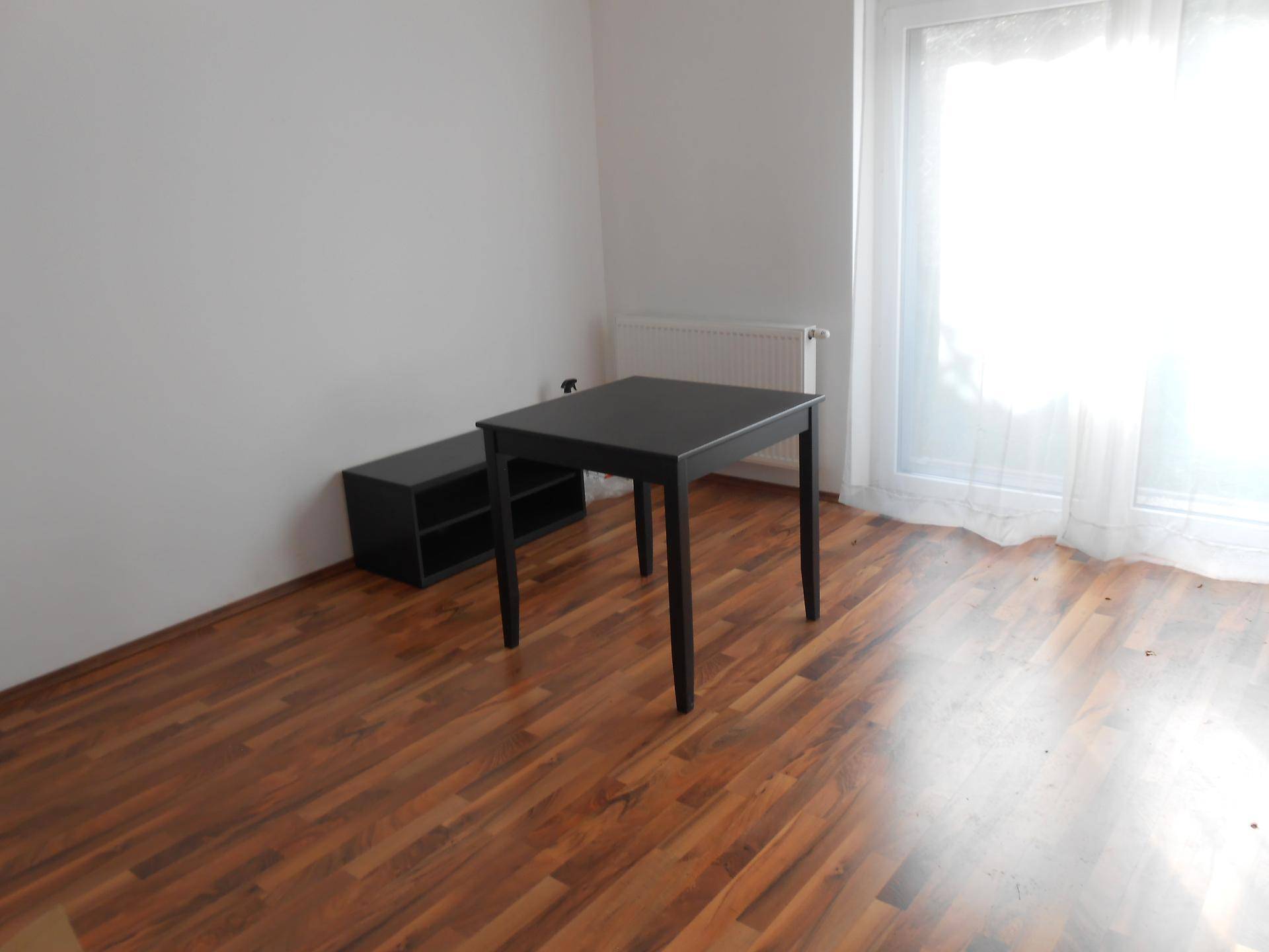 Heller Raum mit kleinem schwarzen Tisch, Holzfußboden und viel Tageslicht.