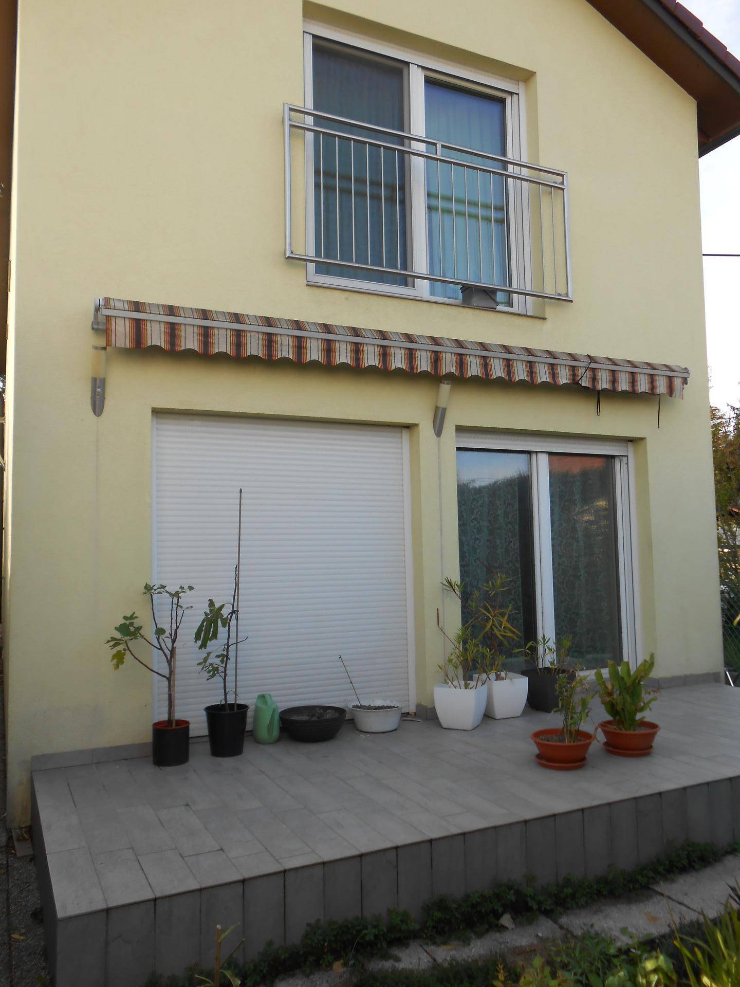 Gelbe Hausfassade mit Balkon, Markise und bepflanzter Terrasse im Erdgeschoss.