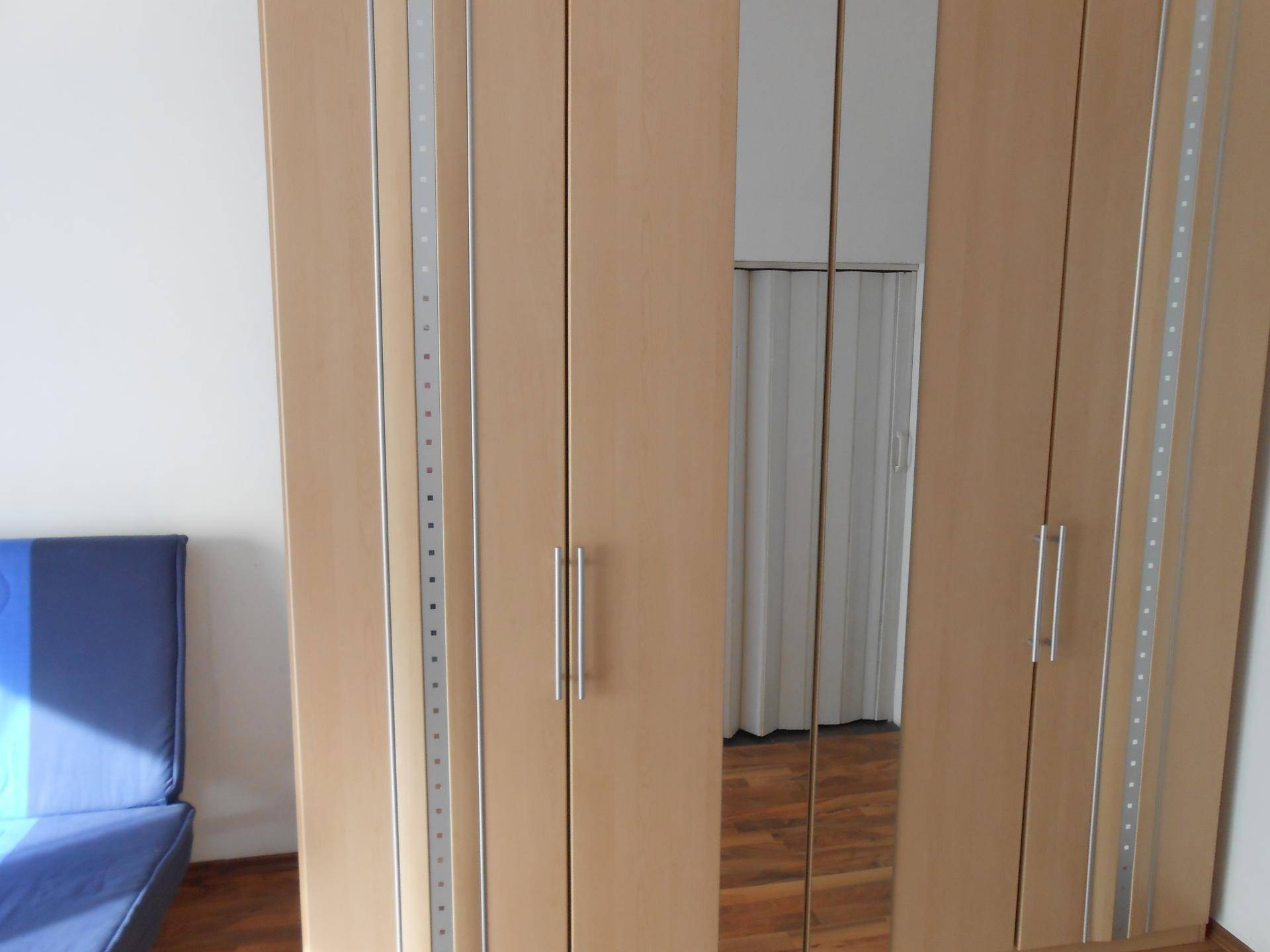 Großer Kleiderschrank mit Spiegeltüren und Holzdekor in einem hellen Raum.
