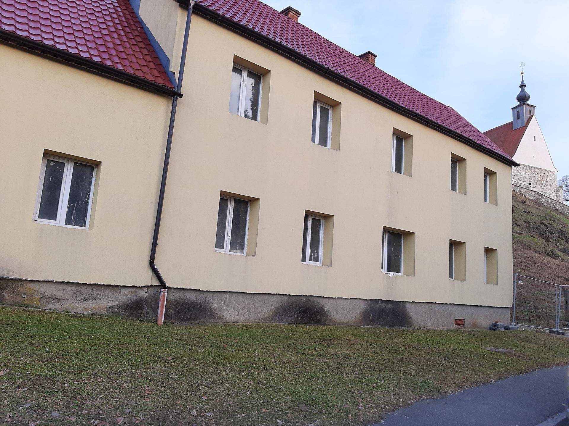 Seitenansicht des gelben Gebäudes mit rotem Dach und einer Kirche im Hintergrund auf dem Hügel.