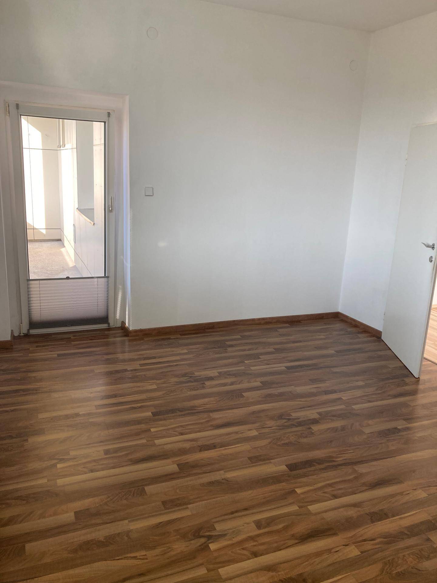 Heller Wohnraum mit Laminatboden und Zugang zu einem Balkon oder einer Terrasse.