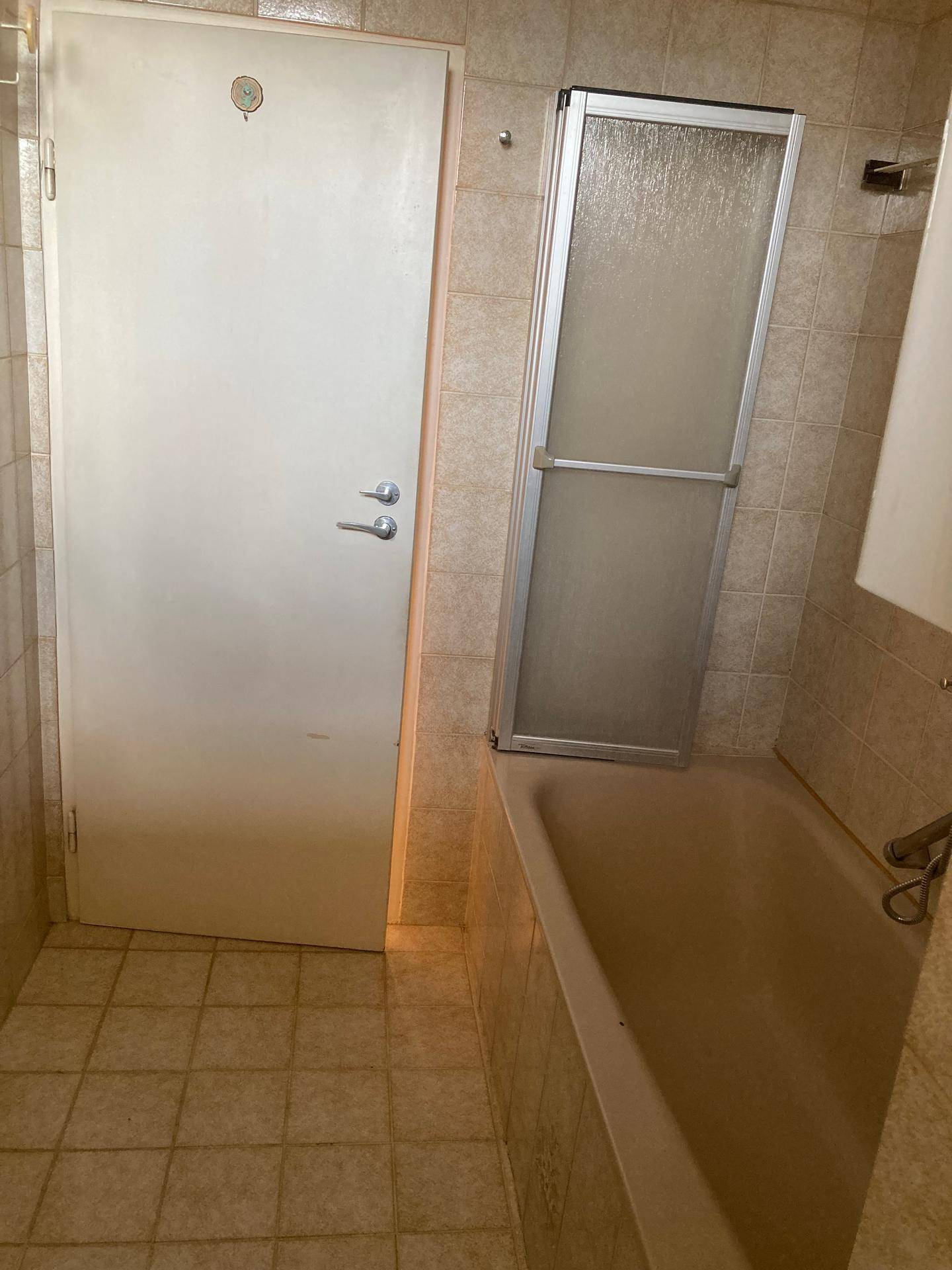 Badezimmer mit Badewanne, Duschabtrennung und hellen Fliesen an Wänden und Boden.