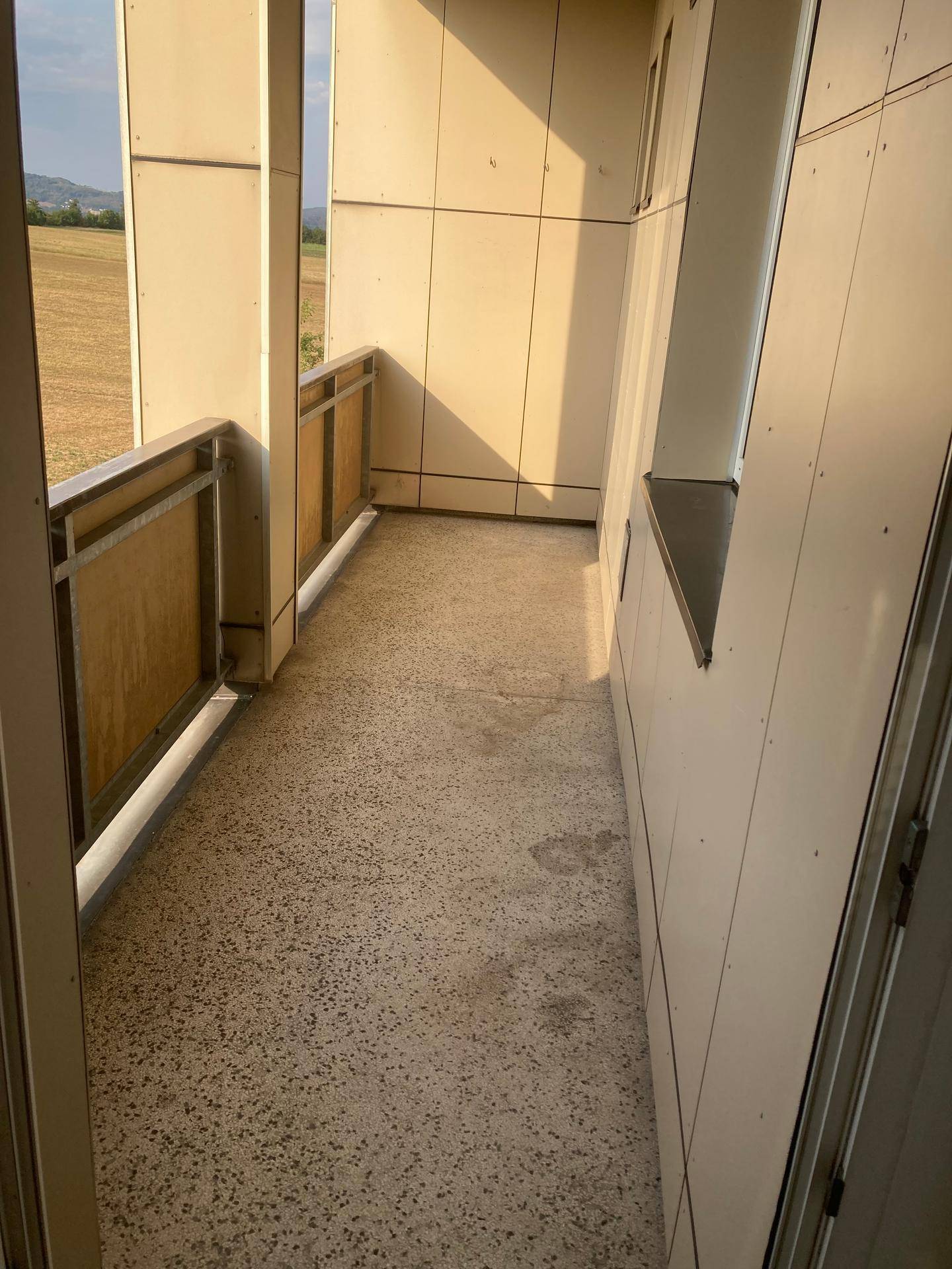 Schmaler Balkon mit Metallgeländer und Blick auf Felder und Hügel.