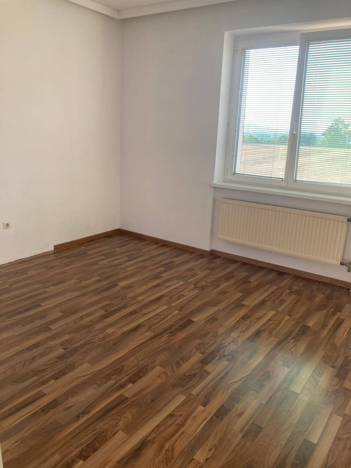 Helles Schlafzimmer mit Laminatboden, Fenster und Blick auf die grüne Umgebung.