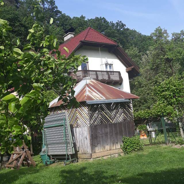 Hausansicht vom Garten aus mit einem kleinen Holzschuppen und viel Grün im Vordergrund.