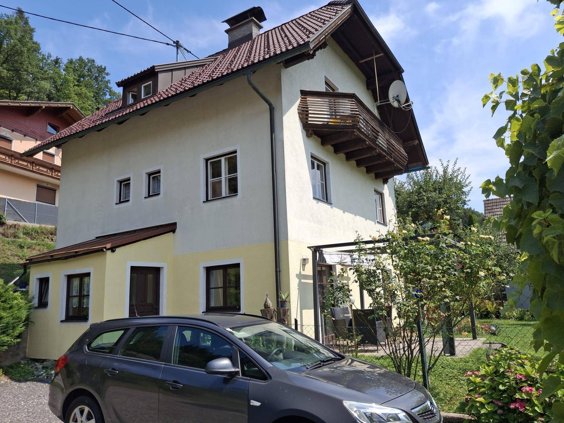 Hausansicht mit gepflegtem Garten, Balkon und einem Auto in der Einfahrt.