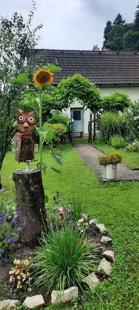 Gepflegter Gartenweg führt zum Haus, geschmückt mit Sonnenblume und Eulenfigur.