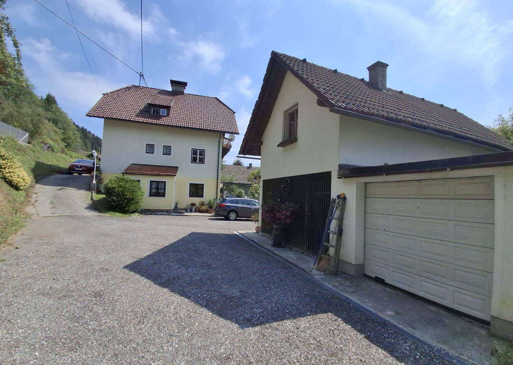 Zwei Häuser mit Schotterzufahrt, umgeben von grüner Hügellandschaft und Garage.