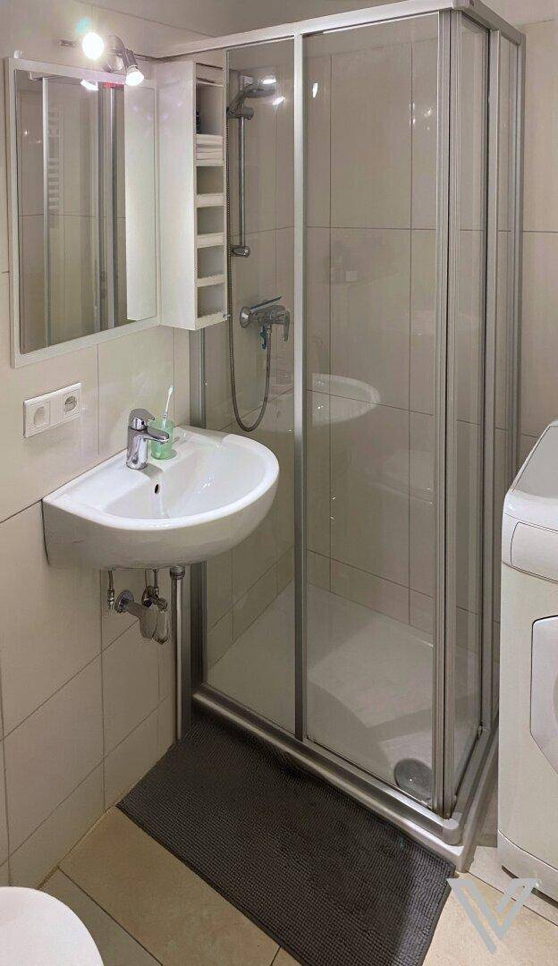 Kleines Badezimmer mit Duschkabine, Waschbecken und Spiegelschrank, komplett gefliest und modern gestaltet.