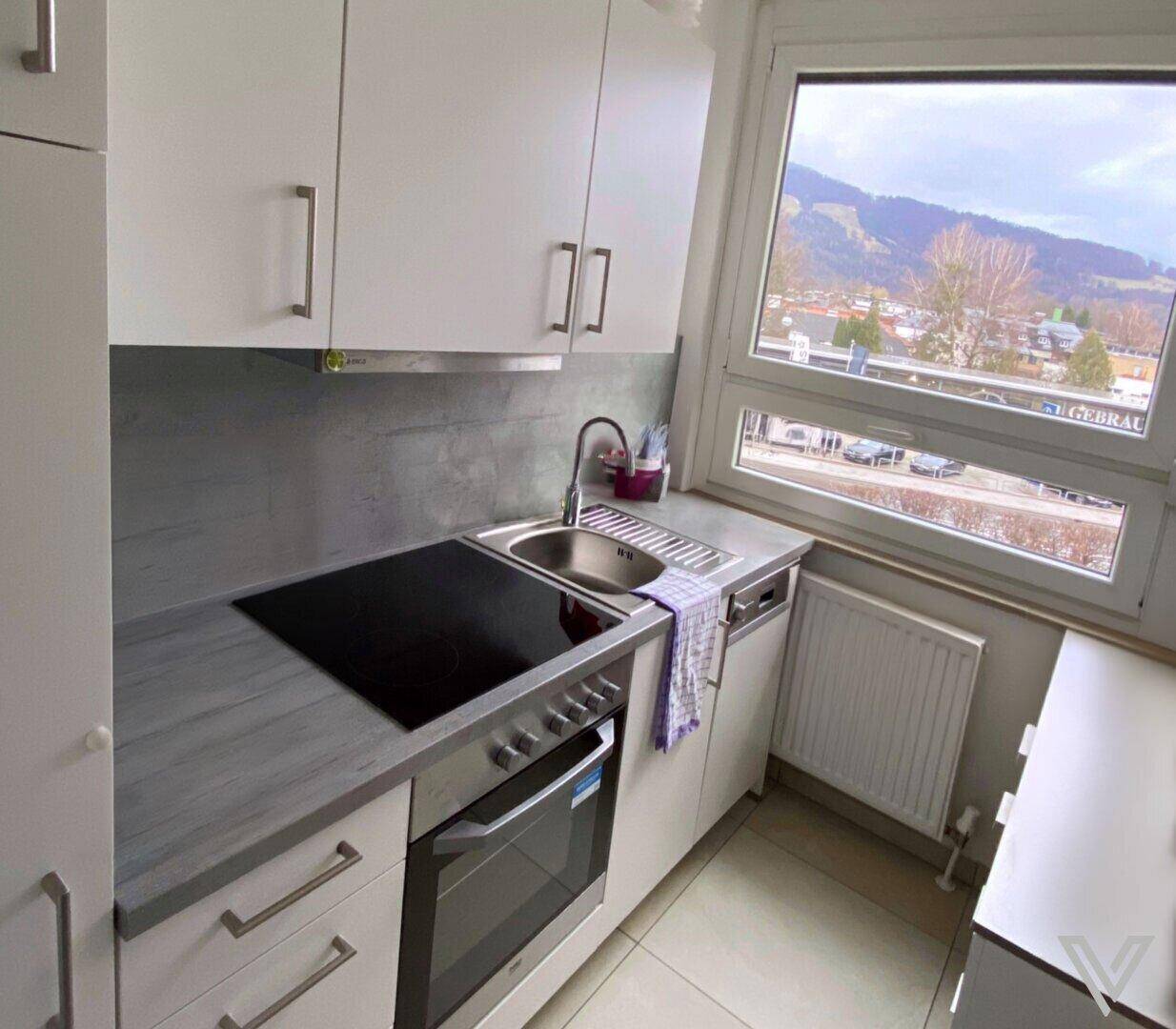 Funktionale Küche mit weißen Schränken, Induktionskochfeld und Bergblick durch das Küchenfenster.