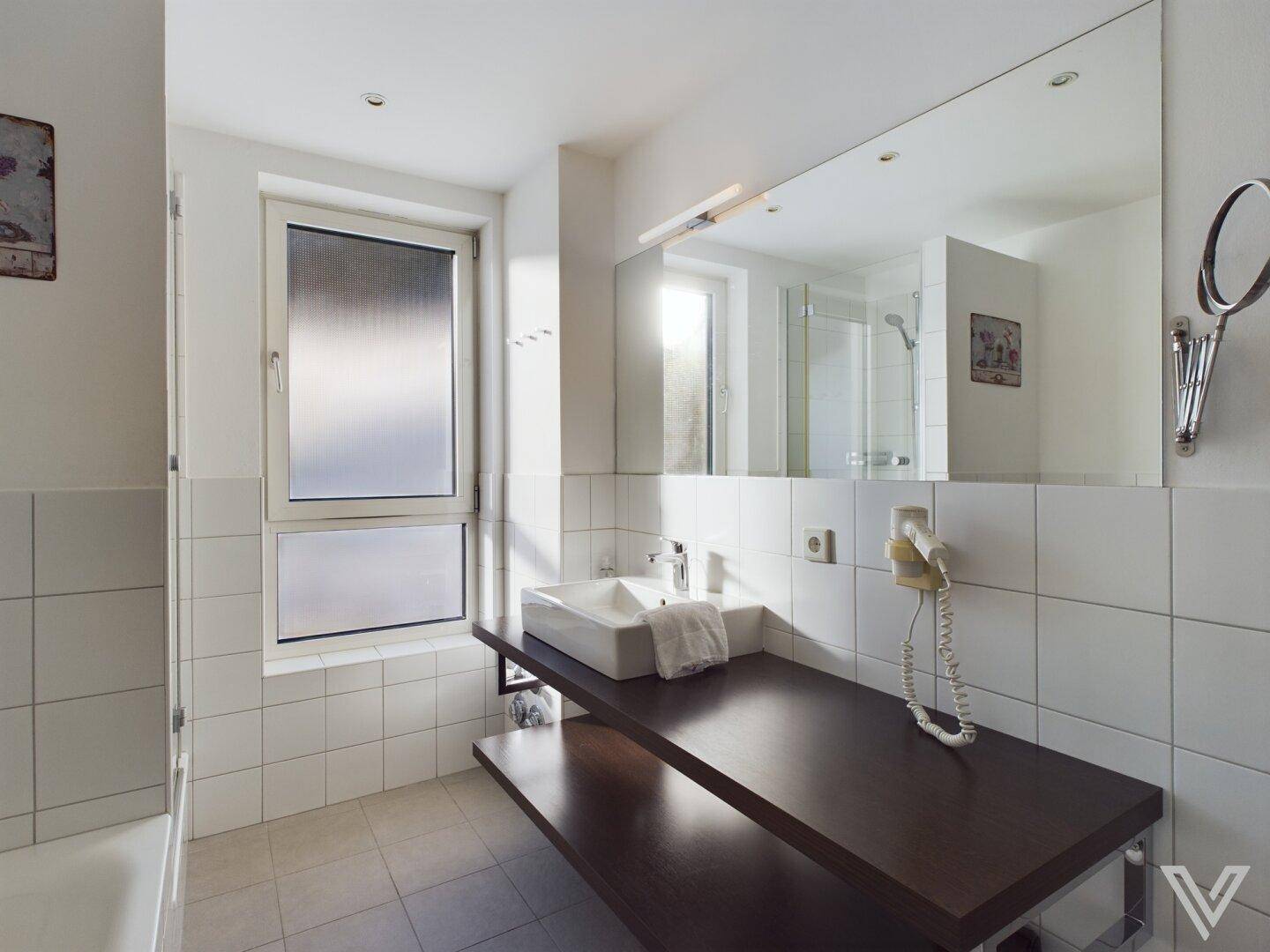 Helles Badezimmer mit großem Spiegel, modernem Waschbecken und Fenster für Tageslicht.