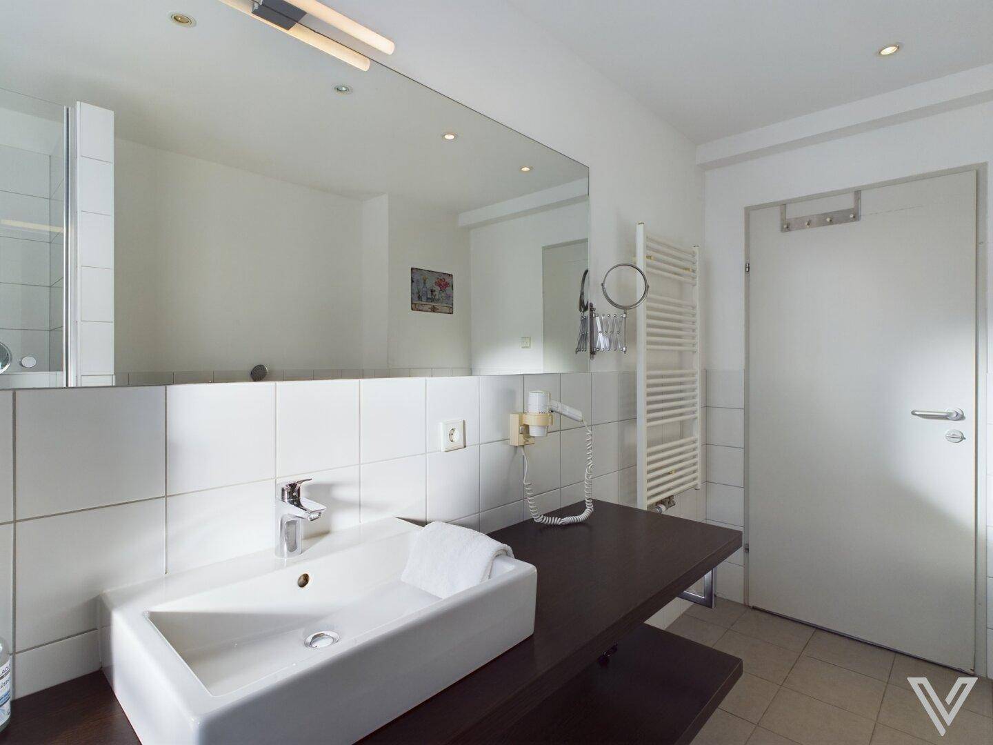 Funktionales Badezimmer mit Waschbecken, großem Spiegel und beheiztem Handtuchhalter.