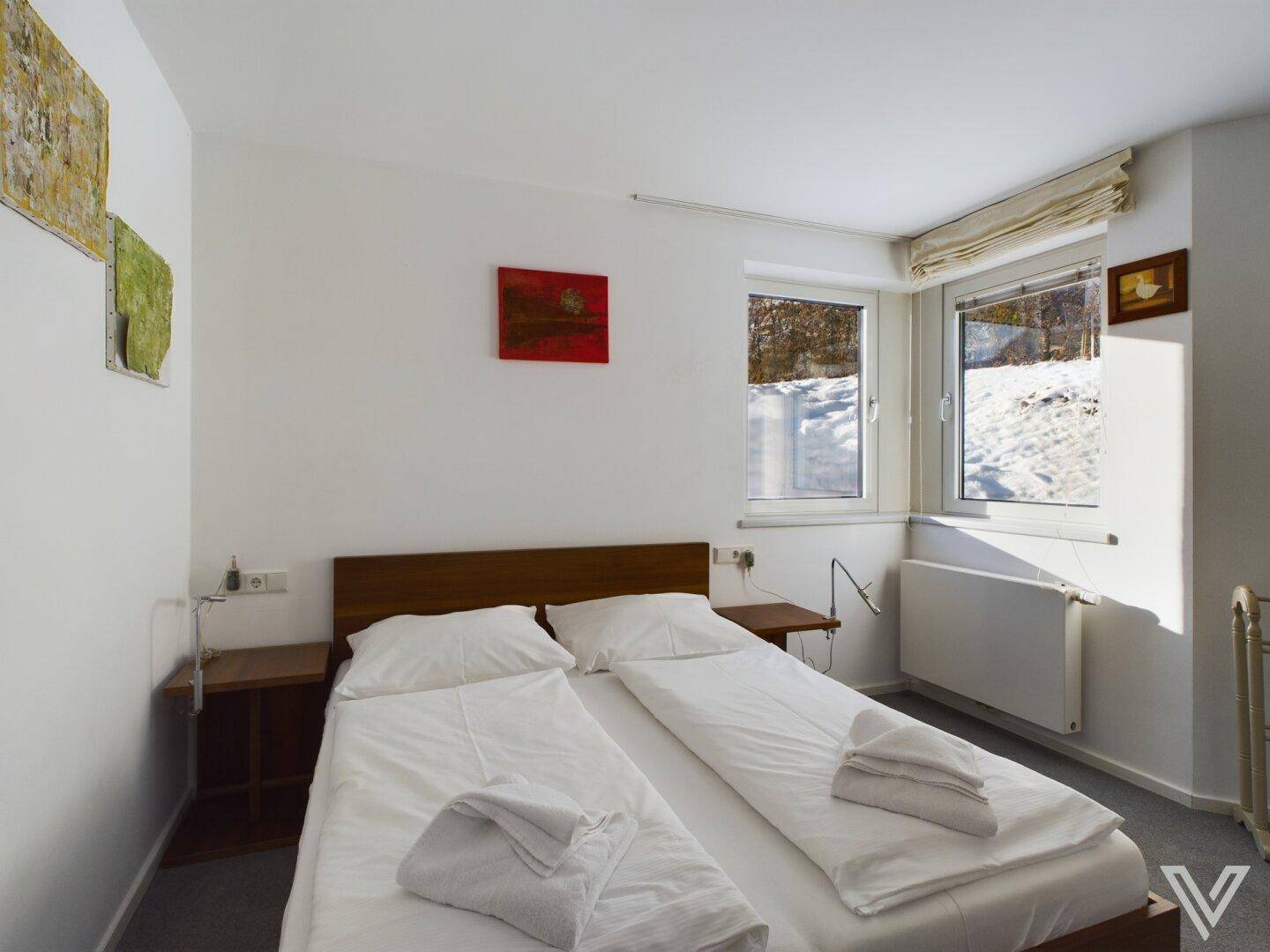 Helles Schlafzimmer mit Doppelbett, Teppichboden und Fenster mit Blick auf die verschneite Umgebung.