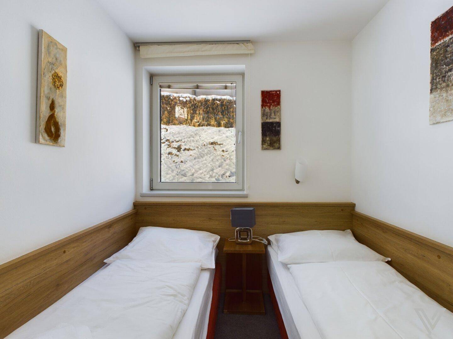 Kleines Schlafzimmer mit zwei Einzelbetten und Fensterblick auf die verschneite Landschaft.