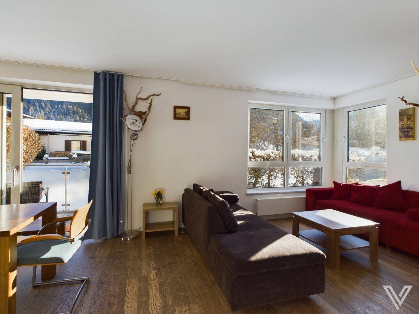 Gemütliches Wohnzimmer mit roten Sofas, Holzboden und großen Fenstern mit Blick auf die verschneite Landschaft.