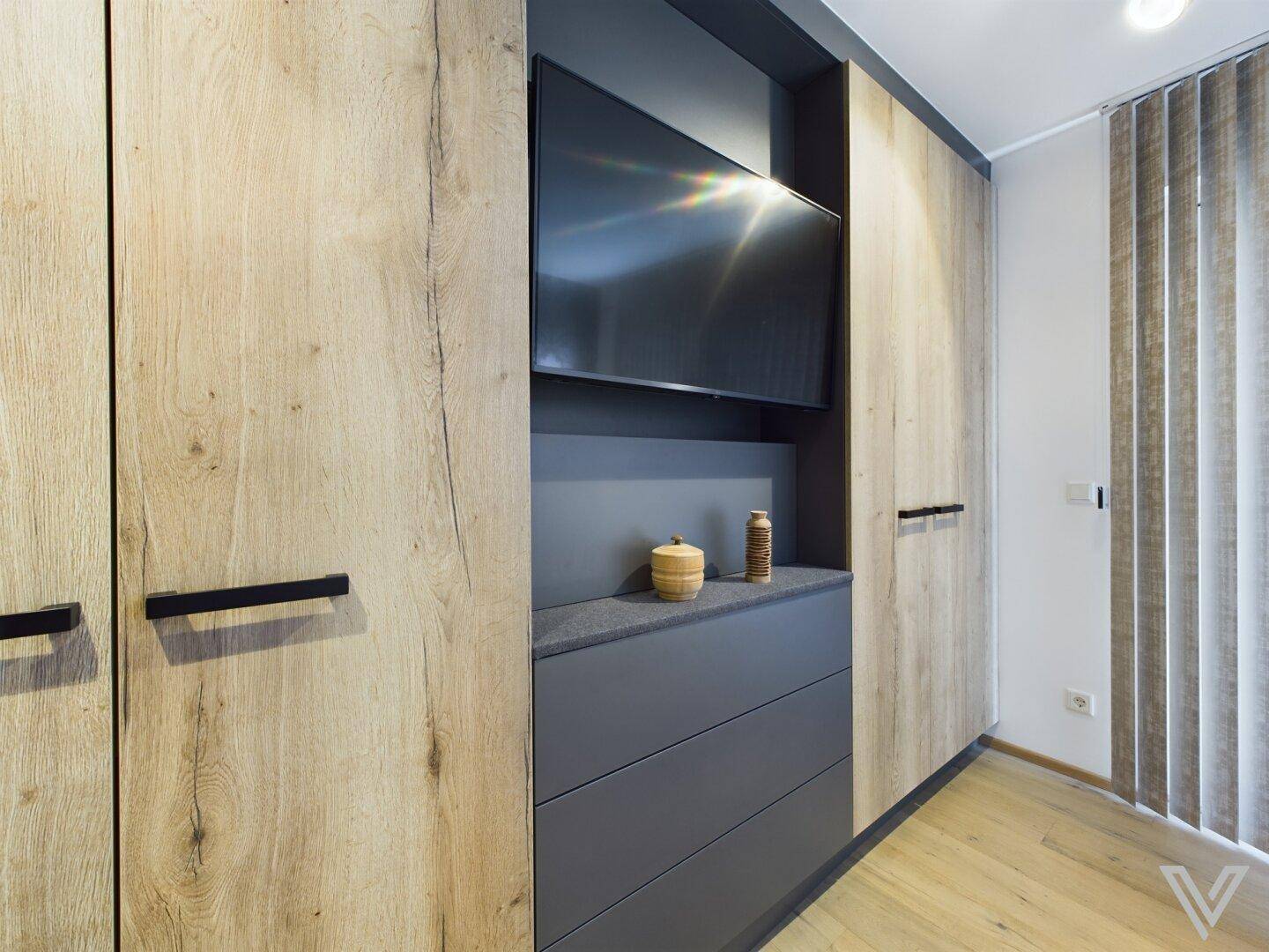 Schlafzimmer mit integriertem Fernseher in den Einbauschränken und Holzboden.