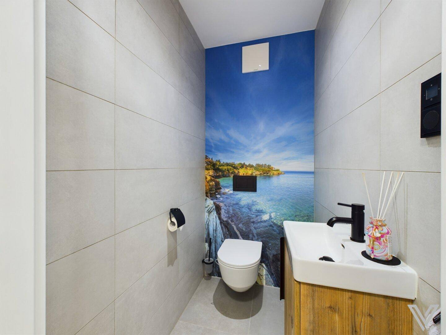 Gäste-WC mit Wand-WC, kleinem Waschbecken und Meerblick-Tapete als Akzentwand.