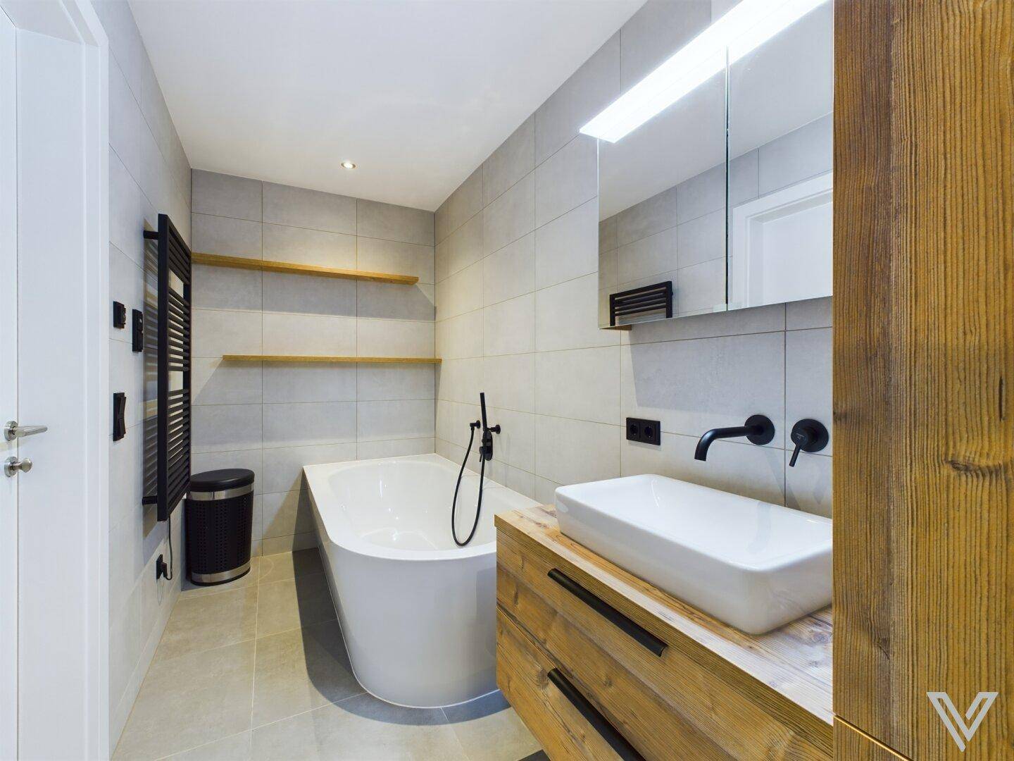 Modernes Badezimmer mit freistehender Badewanne, Holzwaschtisch und dunklen Armaturen.