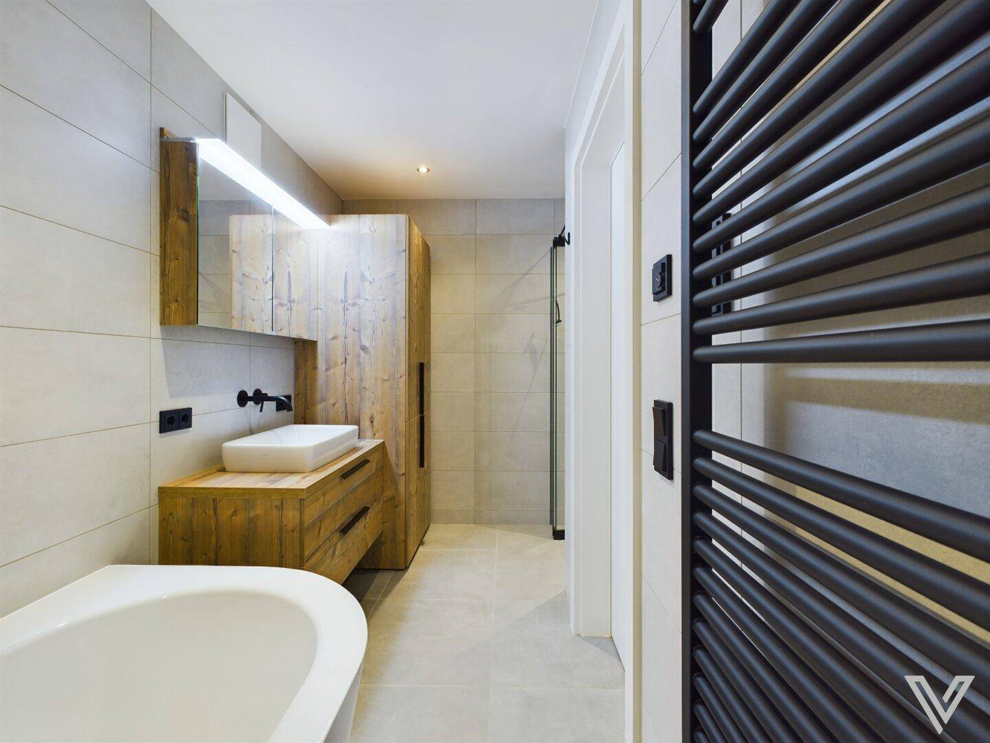 Modernes Badezimmer mit Badewanne, Holzwaschtisch und beheiztem Handtuchhalter.