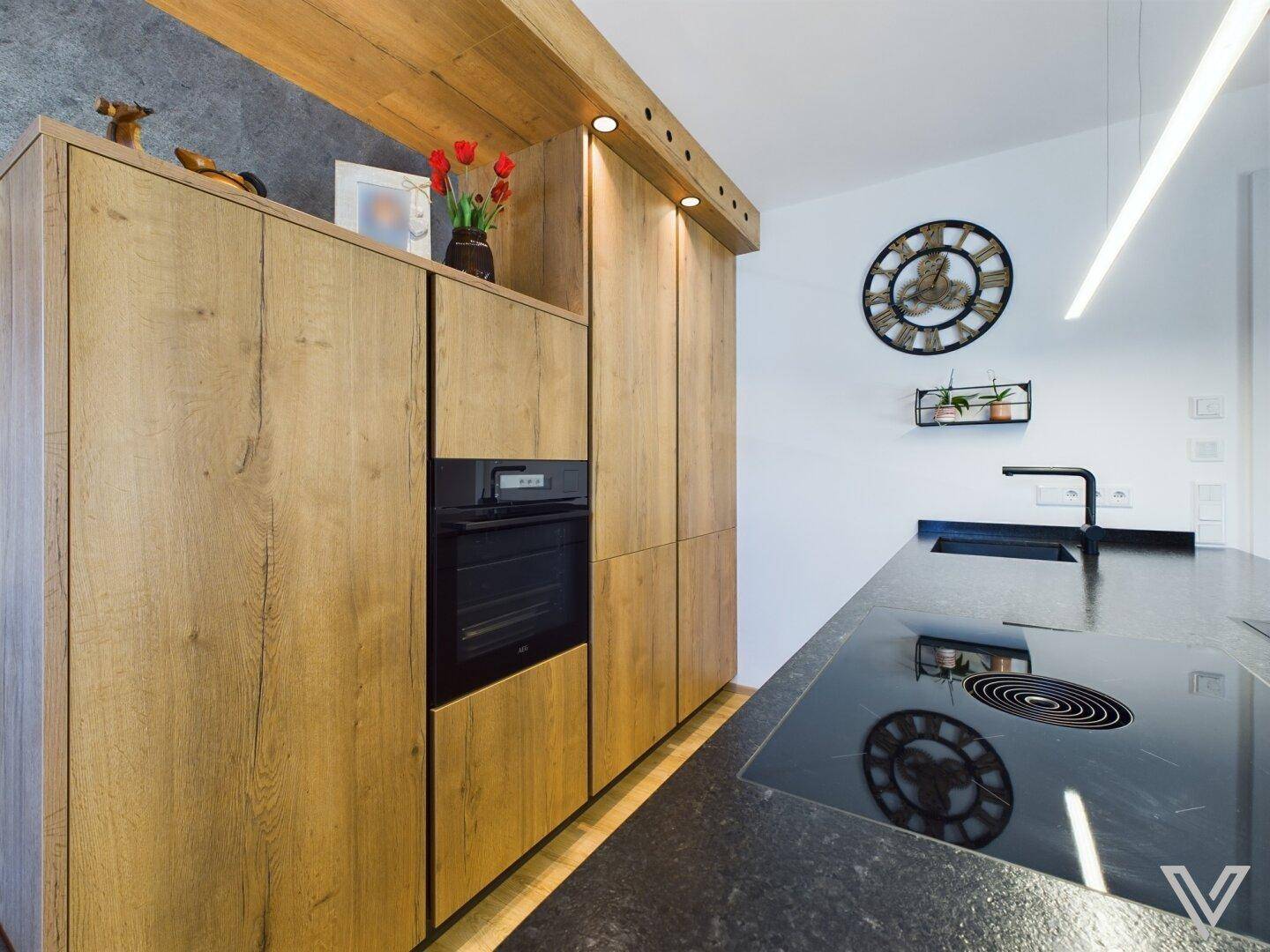 Moderne Küche mit integriertem Backofen, Holzschränken und dunkler Arbeitsplatte.
