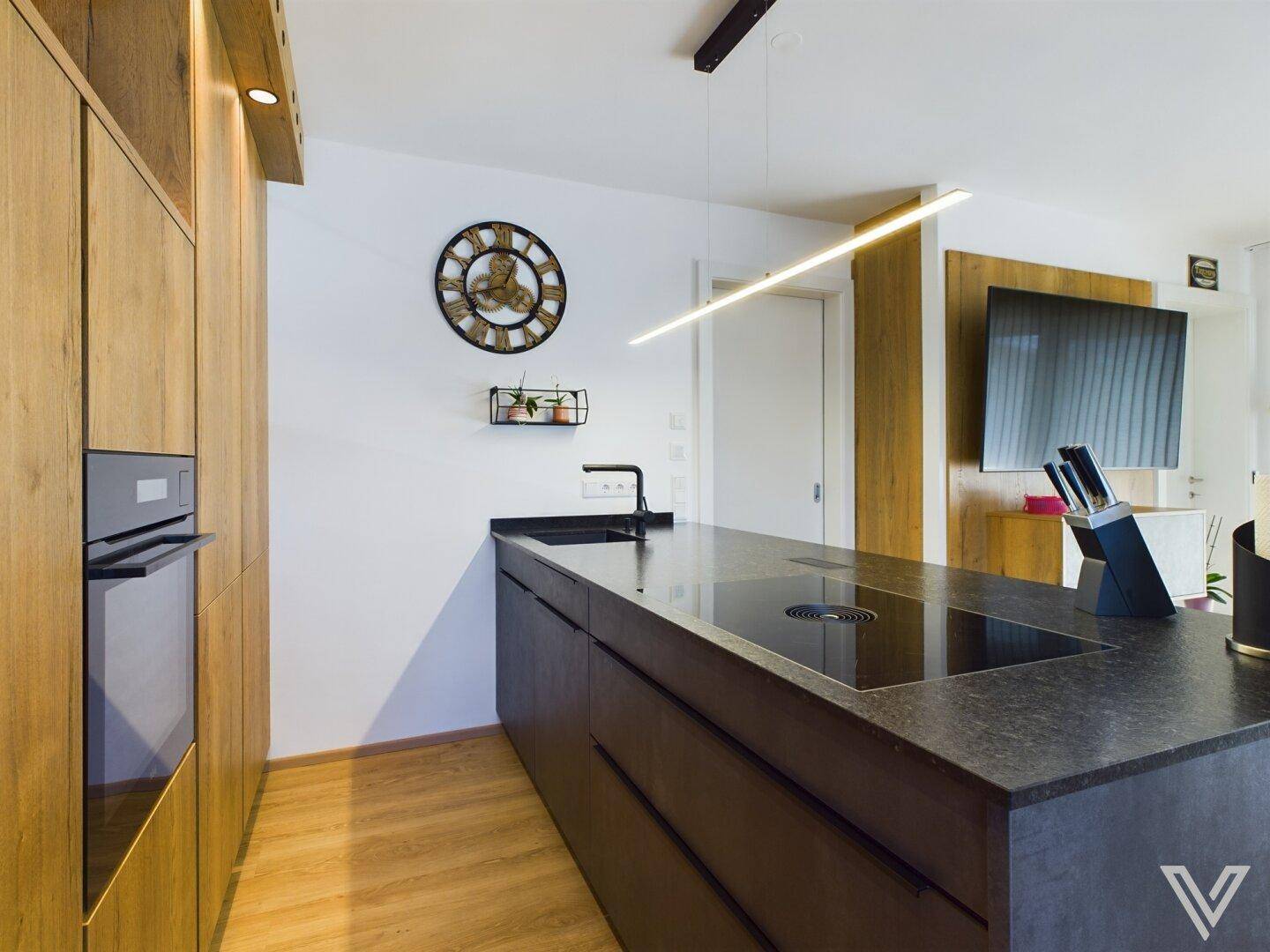 Moderne Küche mit dunkler Arbeitsplatte, integriertem Backofen und Holzschränken.