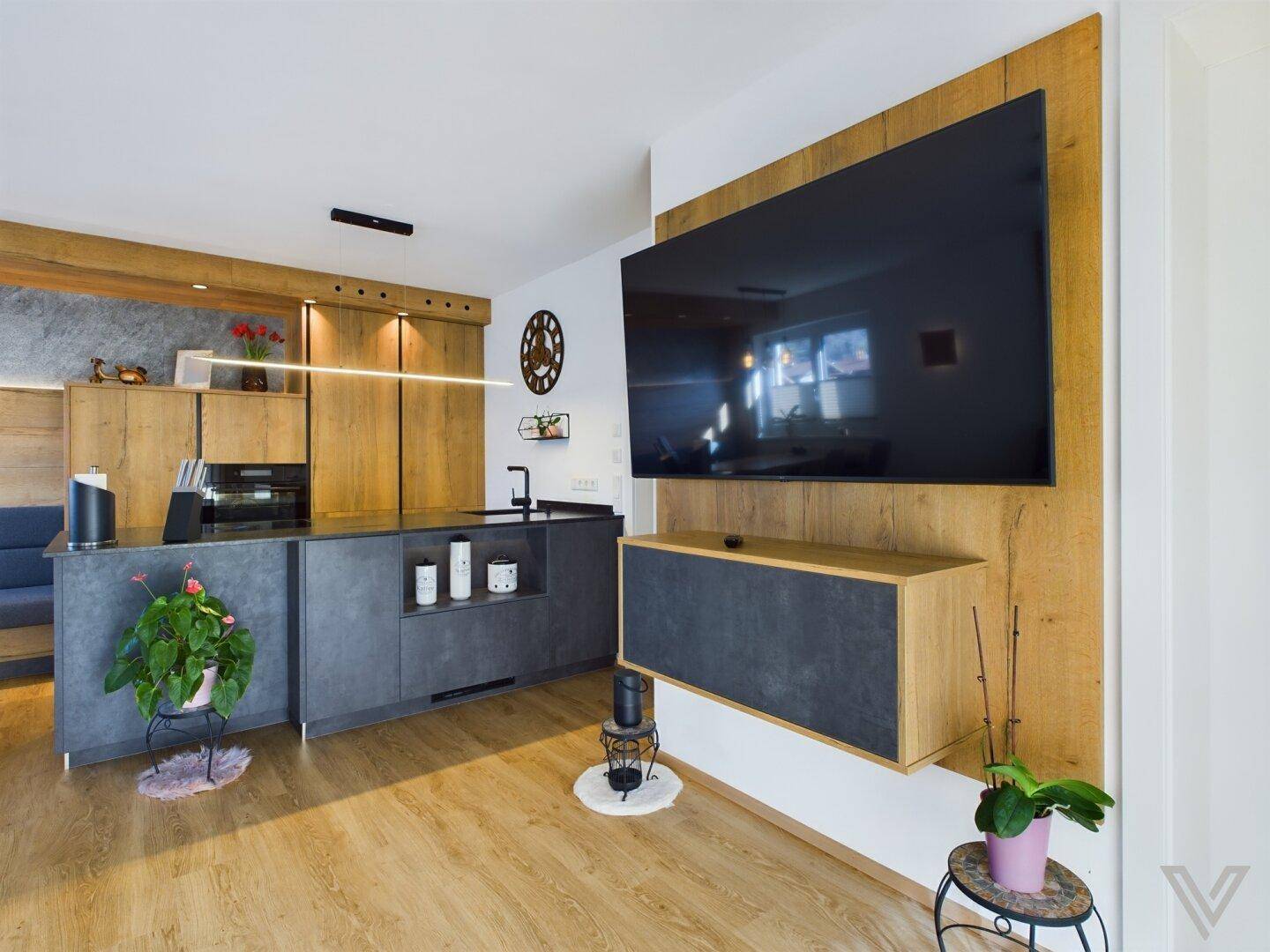 Offene Wohnküche mit Kücheninsel, Holzmöbeln und großem Wandfernseher in modernem Design.