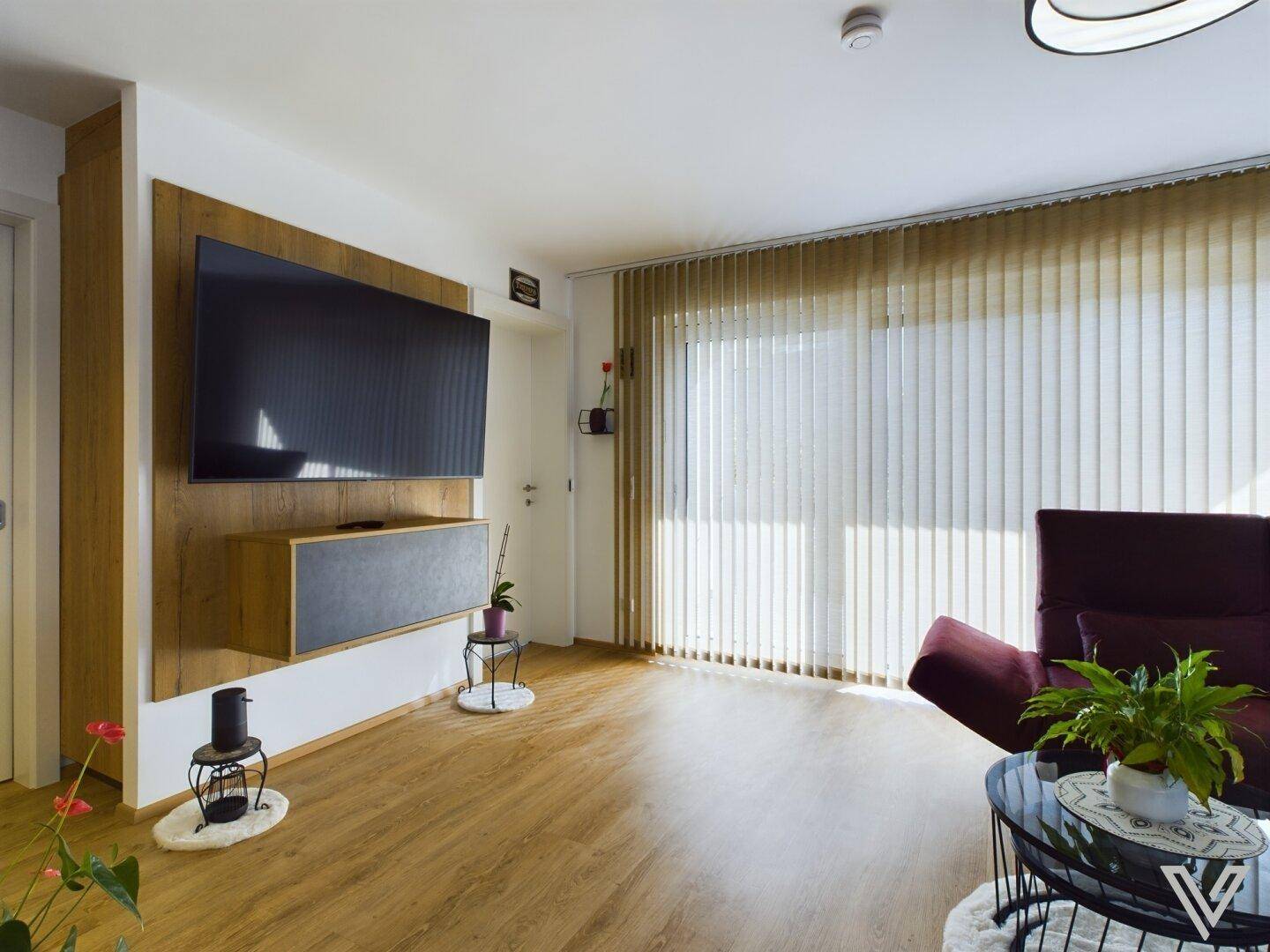 Helles Wohnzimmer mit großem Fernseher, moderner Couch und Zugang zur Terrasse.