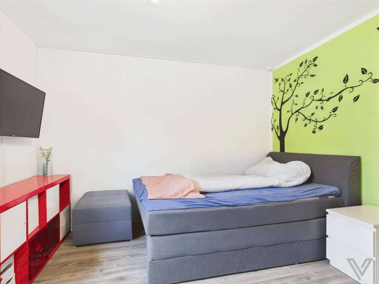 Schlafzimmer mit Boxspringbett, grüner Akzentwand und Fernseher.