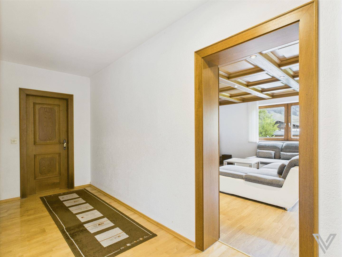 Heller Flur mit Holzfußboden und Zugang zu einem Wohnzimmer mit Holzkassettendecke.