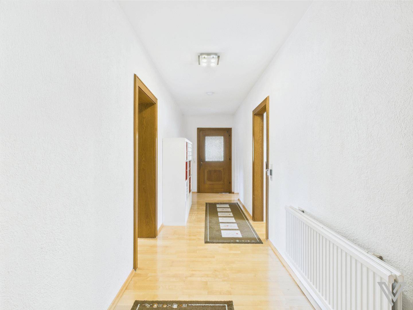 Heller Flur mit Holzfußboden, weißen Wänden und Heizkörper.