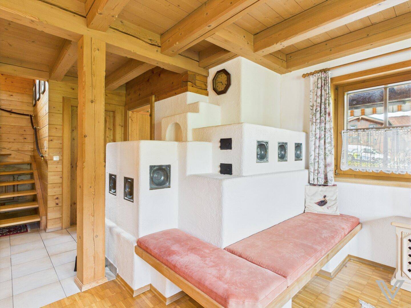 Traditioneller Wohnbereich mit Kachelofen, Holzbalkendecke und gemütlicher Sitzbank am Fenster.
