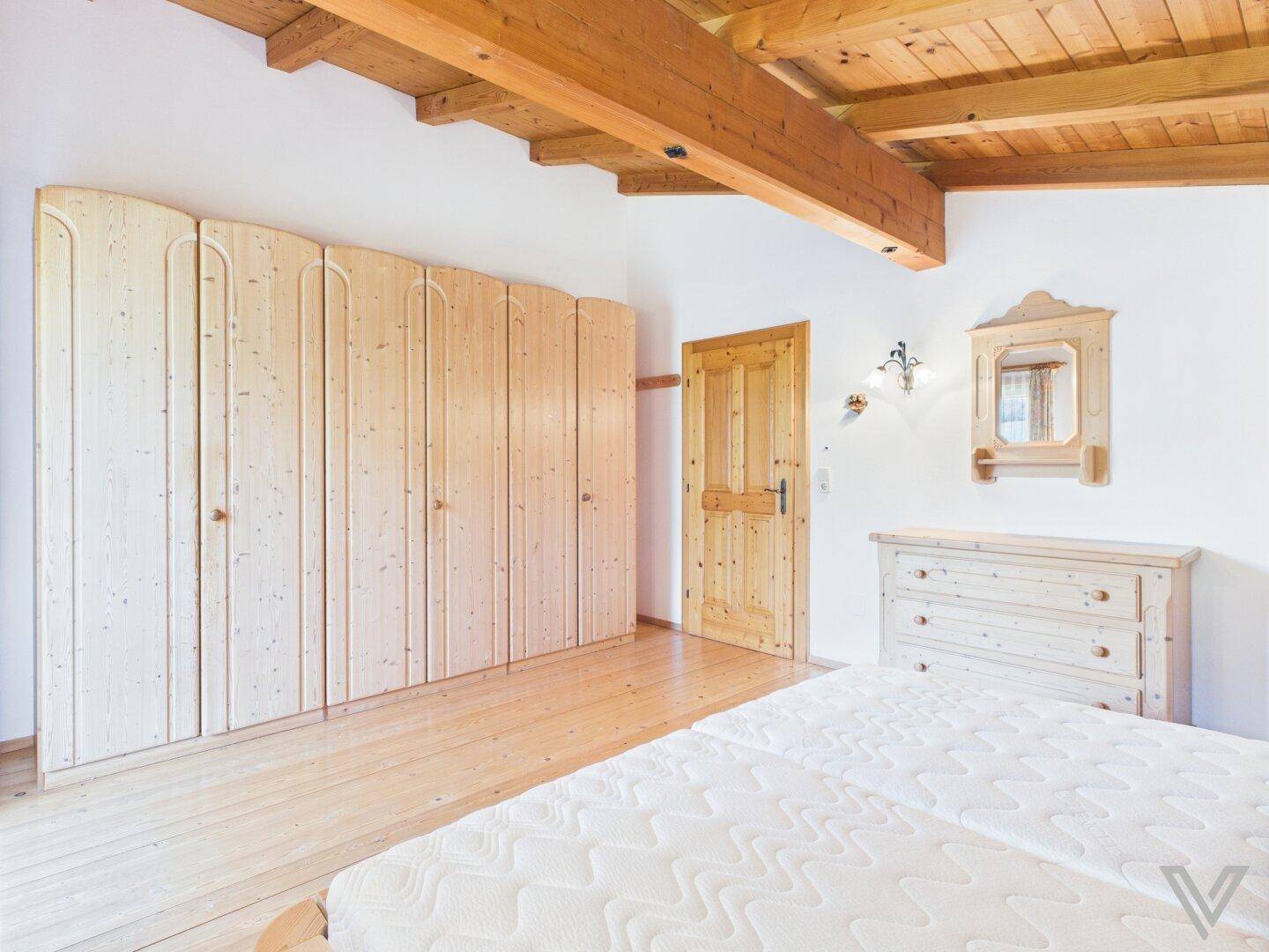 Schlafzimmer mit Einbauschränken, Holzbalkendecke und schrägen Wänden im Dachgeschoss.