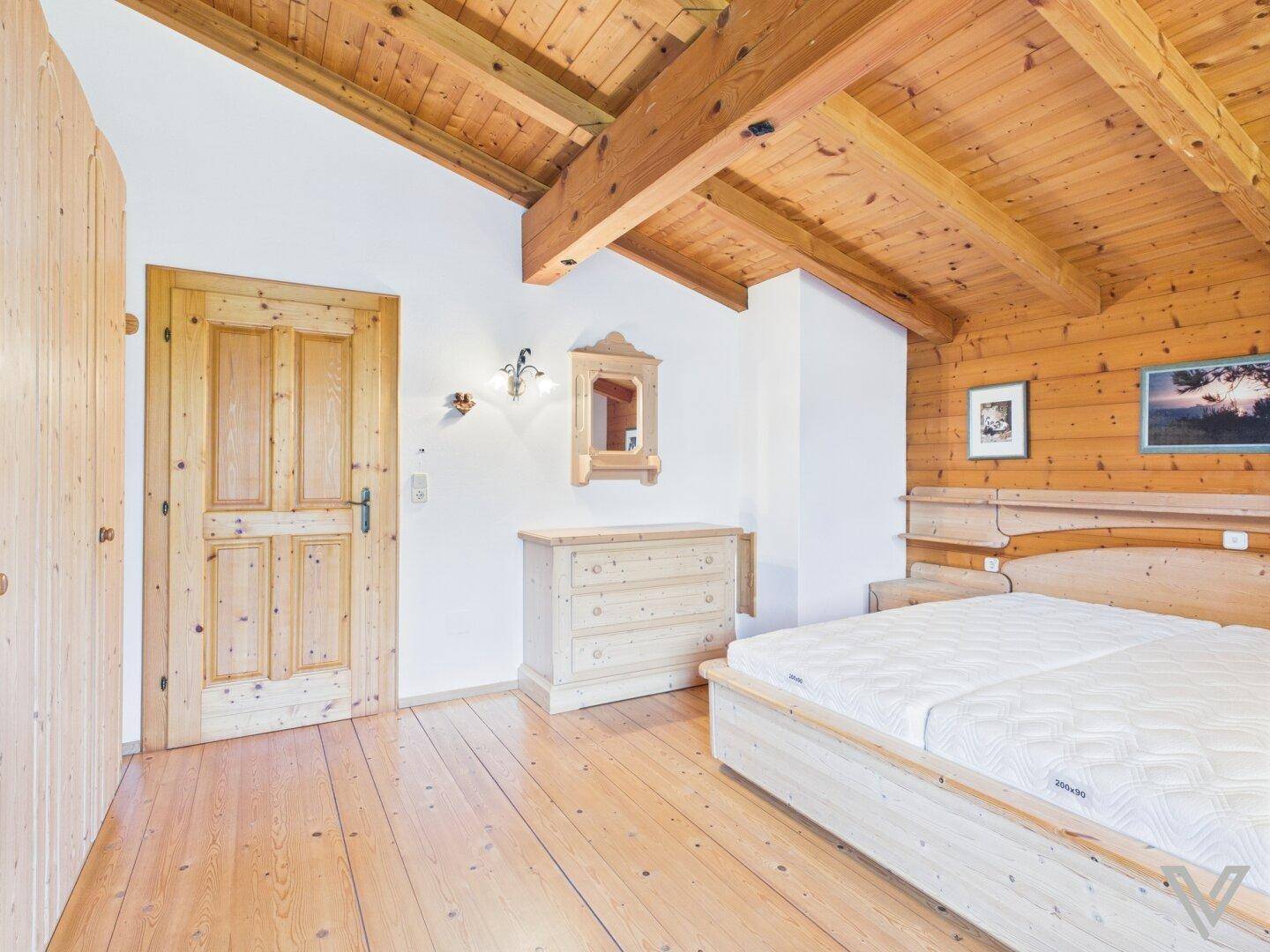 Schlafzimmer mit Holzbett, Kommode und Holzbalkendecke im alpinen Stil.