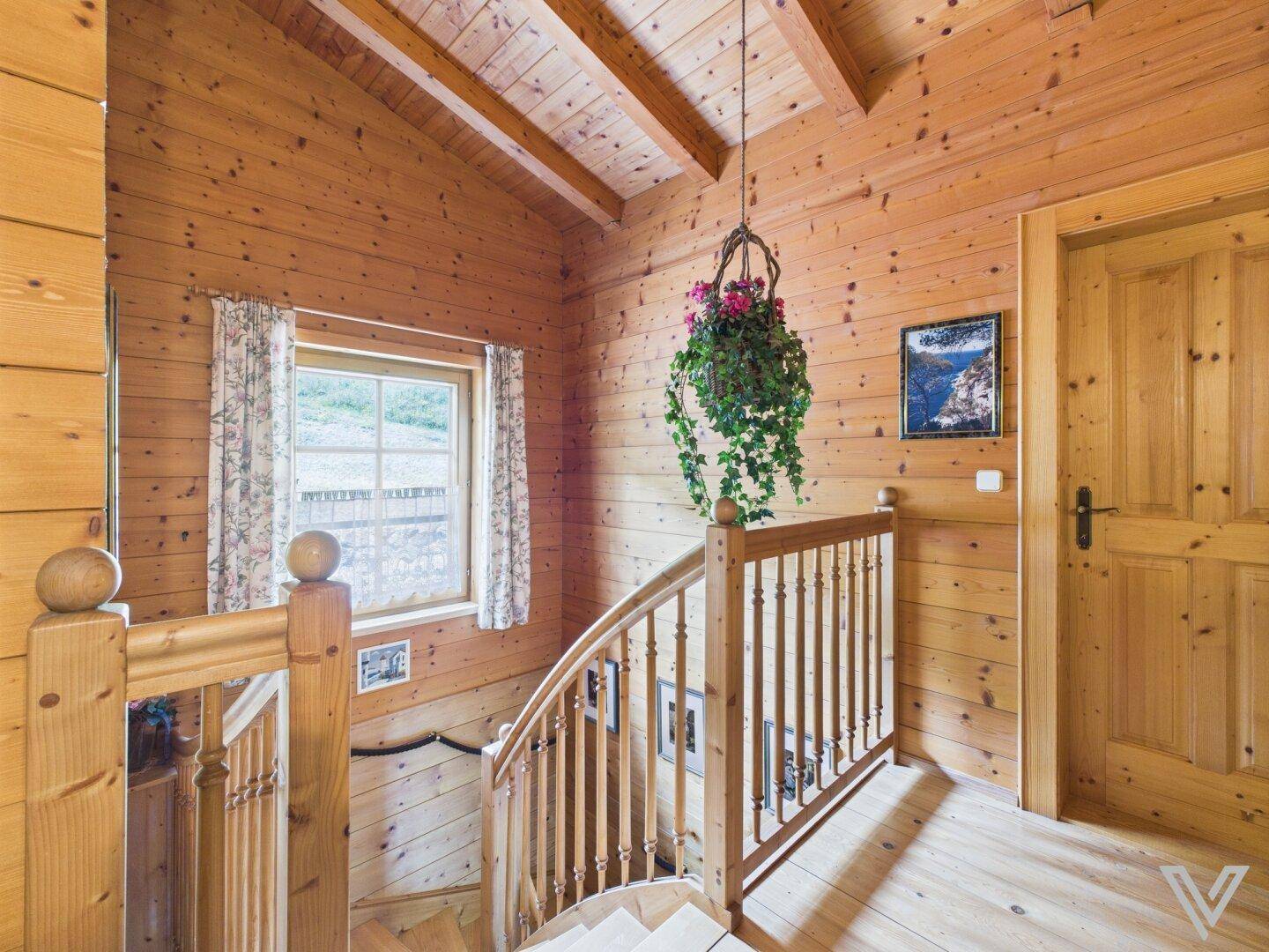 Treppenhaus mit Holzgeländer, Holzwänden und Holzbalkendecke im alpinen Stil.