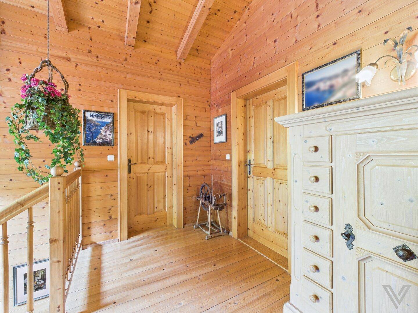 Heller Flur im Obergeschoss mit Holzwänden, Holzbalkendecke und traditionellem Schrank.