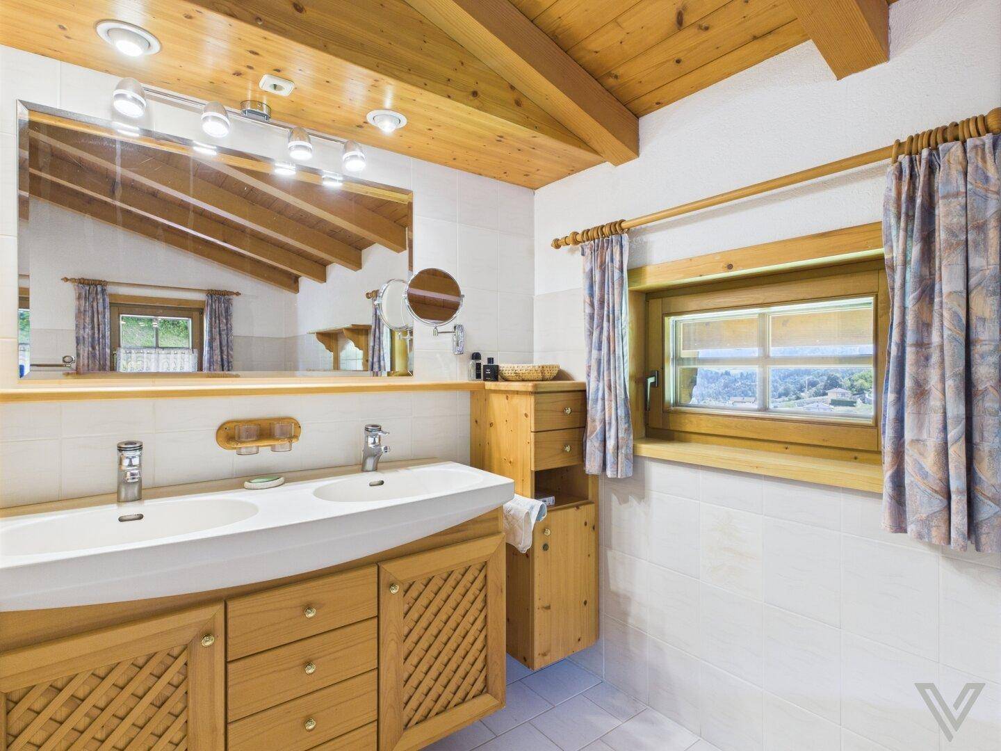 Helles Badezimmer mit Doppelwaschbecken, Spiegel und Holzbalkendecke.