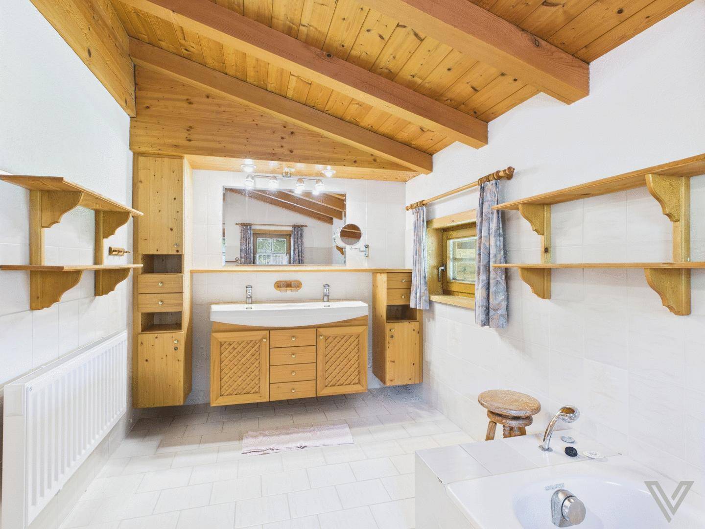 Geräumiges Badezimmer mit Doppelwaschbecken, Badewanne und Holzbalkendecke.